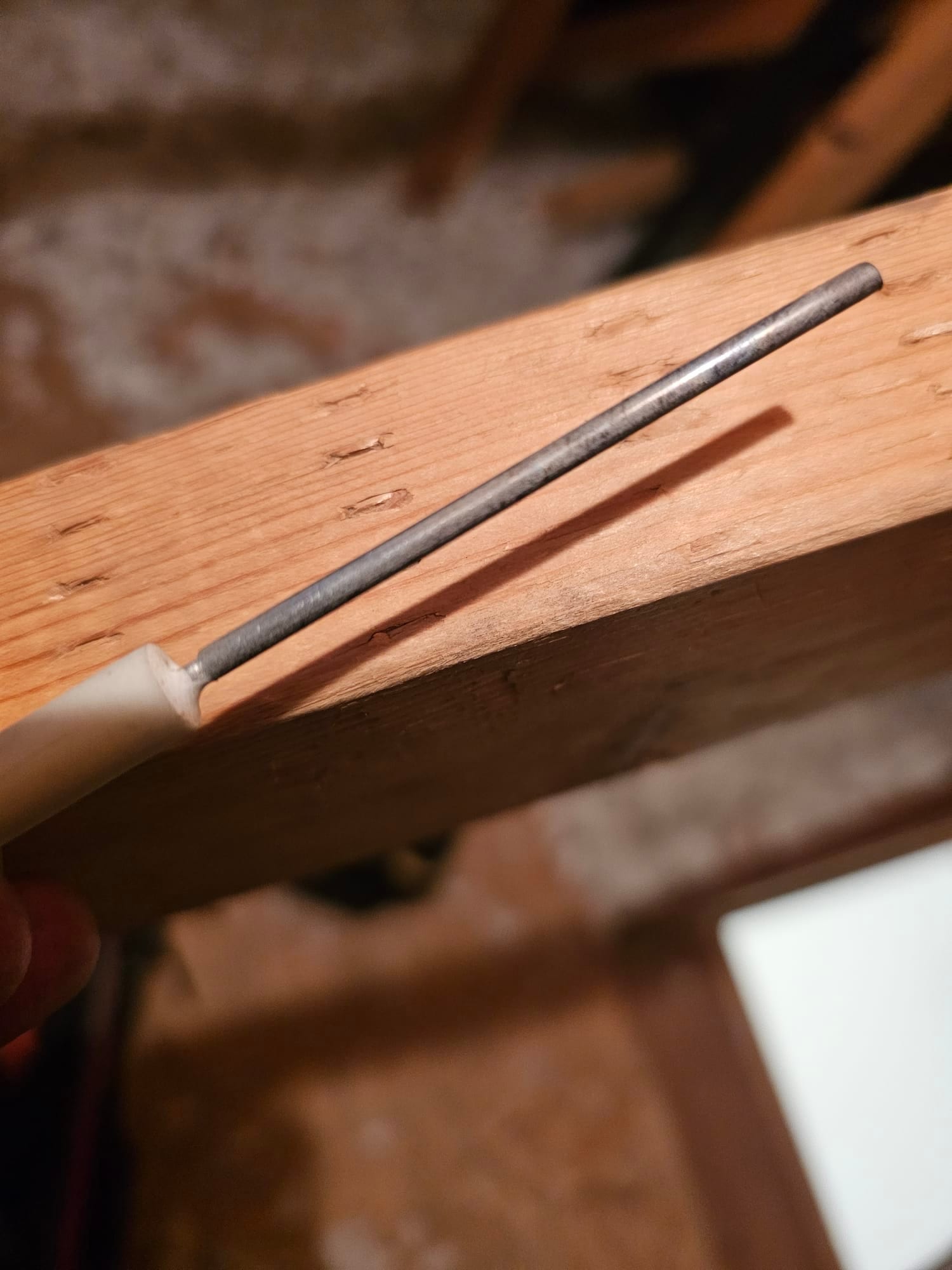 Flame sensor rod with ceramic insulator, held by hand near a wooden beam.