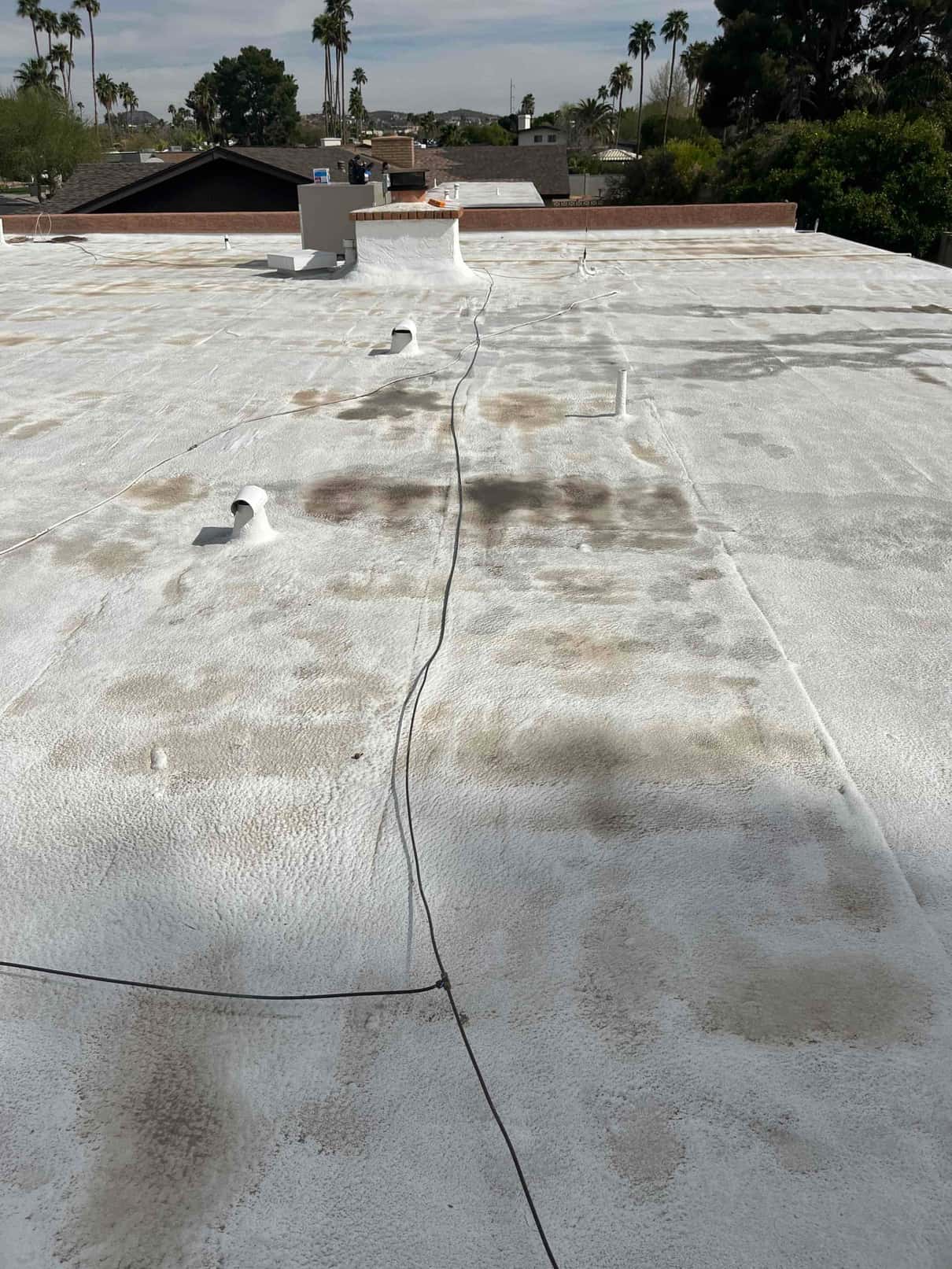Flat roof with rooftop HVAC package unit near parapet and a long cable run laid across the coated surface.