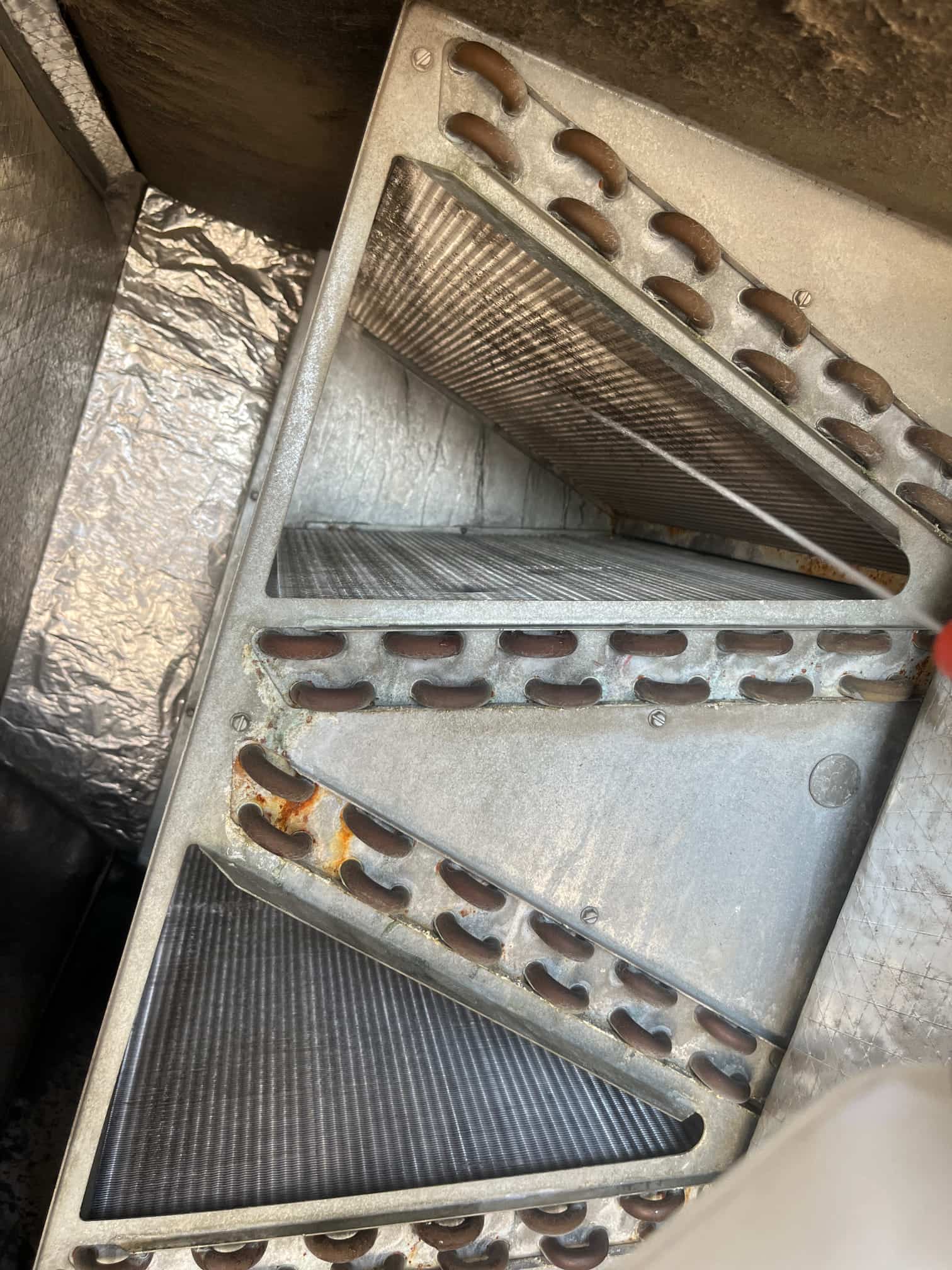 A-frame evaporator coil inside plenum, showing copper U-bend headers and finned coils with visible surface rust at joints.