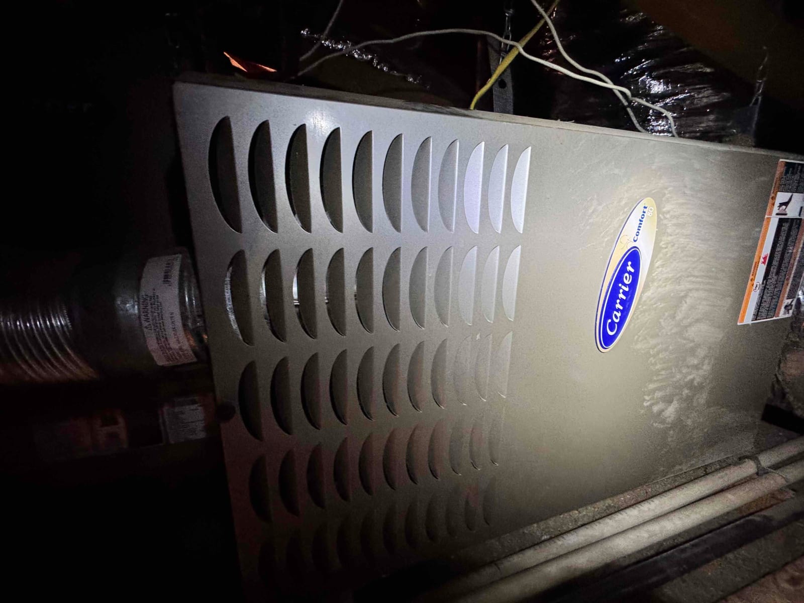 Furnace cabinet with louvered front panel, connected metal vent pipe, and PVC condensate drain lines in attic.