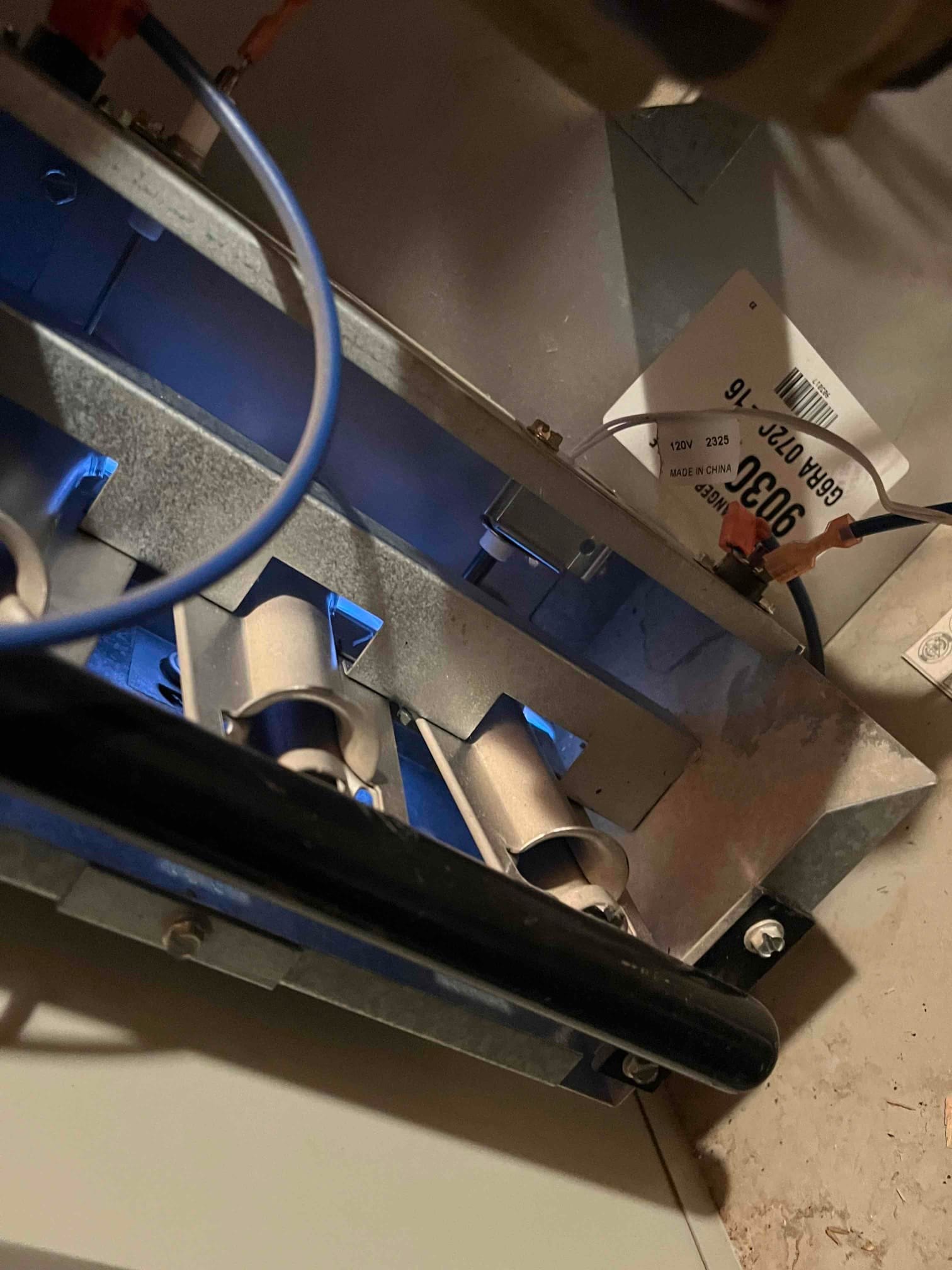 Gas furnace burner section with three tubular burners lit, showing blue flames and nearby wiring.