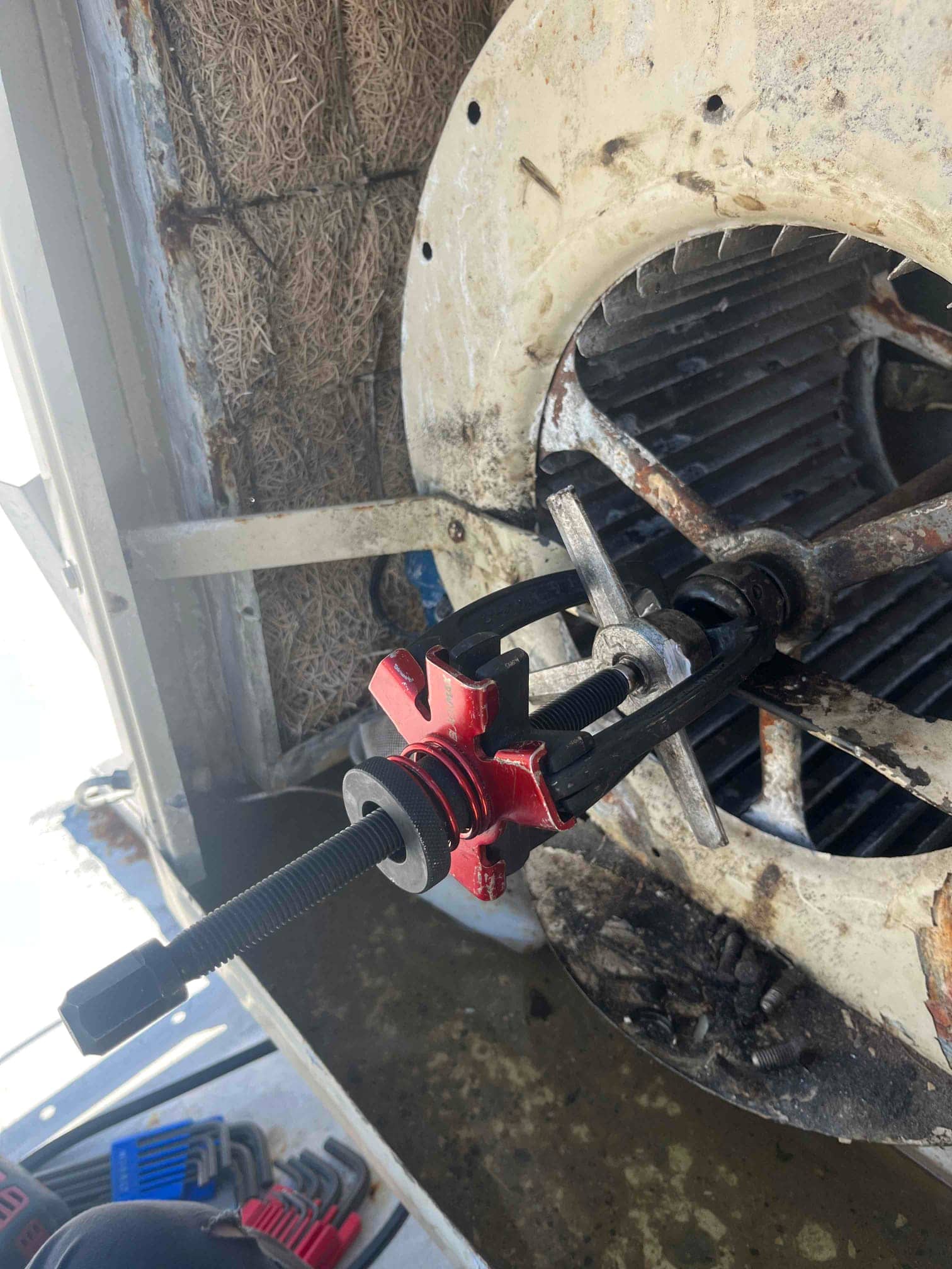 Gear puller is attached to the blower wheel hub inside the housing, with rust and debris around the assembly.