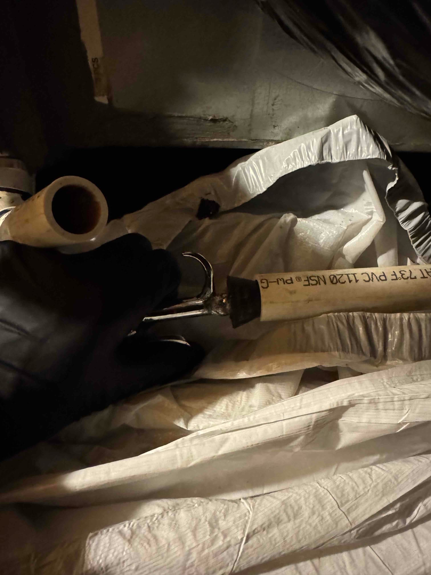 Gloved hand holds a section of PVC piping near the base of an indoor HVAC cabinet.
