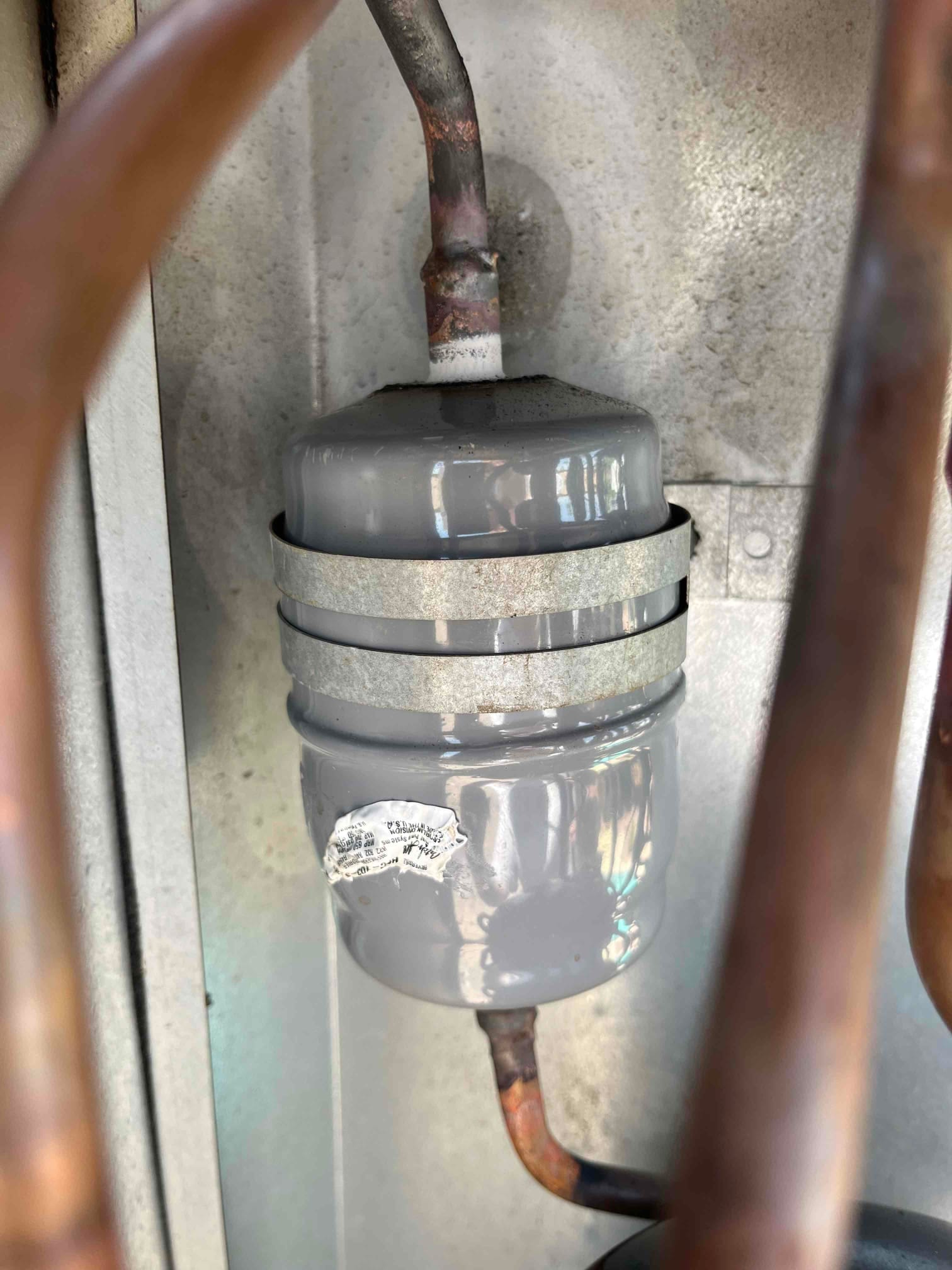 Gray cylindrical canister in the refrigerant line with brazed copper connections and a mounting strap, showing heat discoloration at joints.