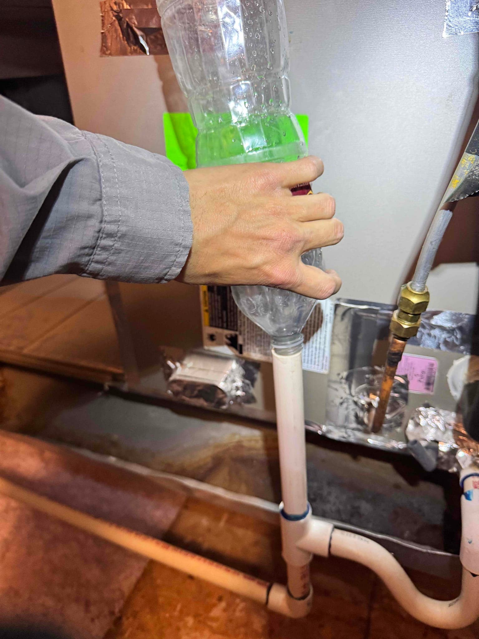 Hand holds a plastic bottle at the condensate drain cleanout on the indoor air handler cabinet.