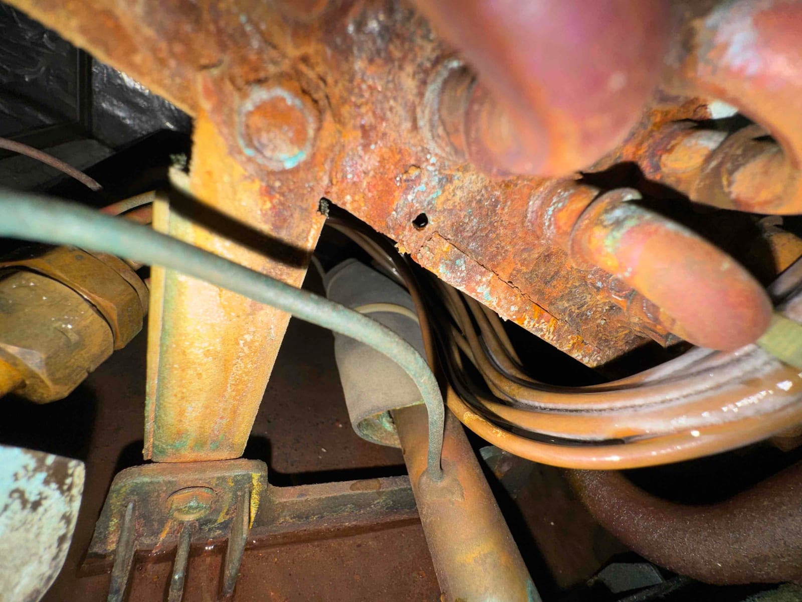 Heavily rusted steel bracket and corroded copper refrigerant tubing with oxidation visible inside the equipment compartment.