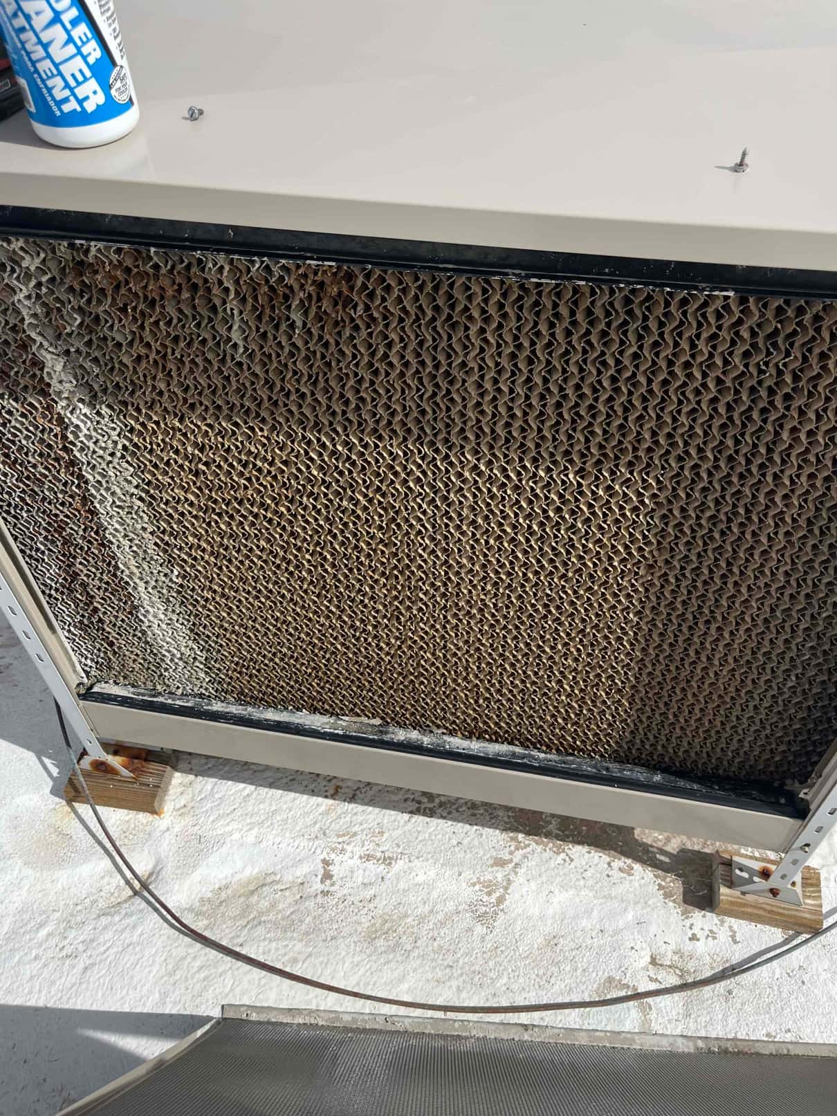 Honeycomb evaporative cooler pad mounted in a rooftop housing, with rust on lower brackets and frame.
