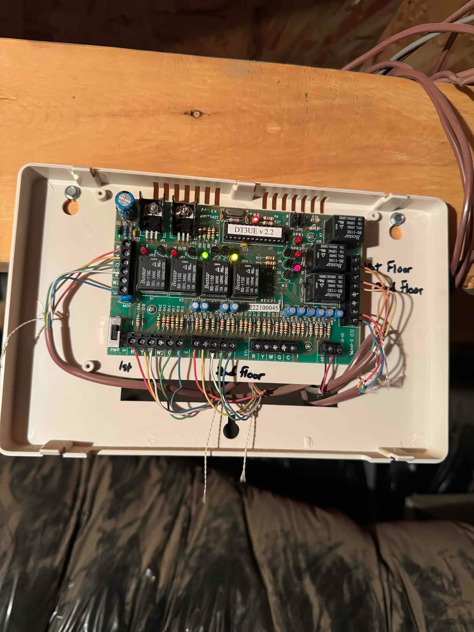 HVAC control board mounted in a plastic enclosure with multiple low-voltage wires connected and status LEDs illuminated.