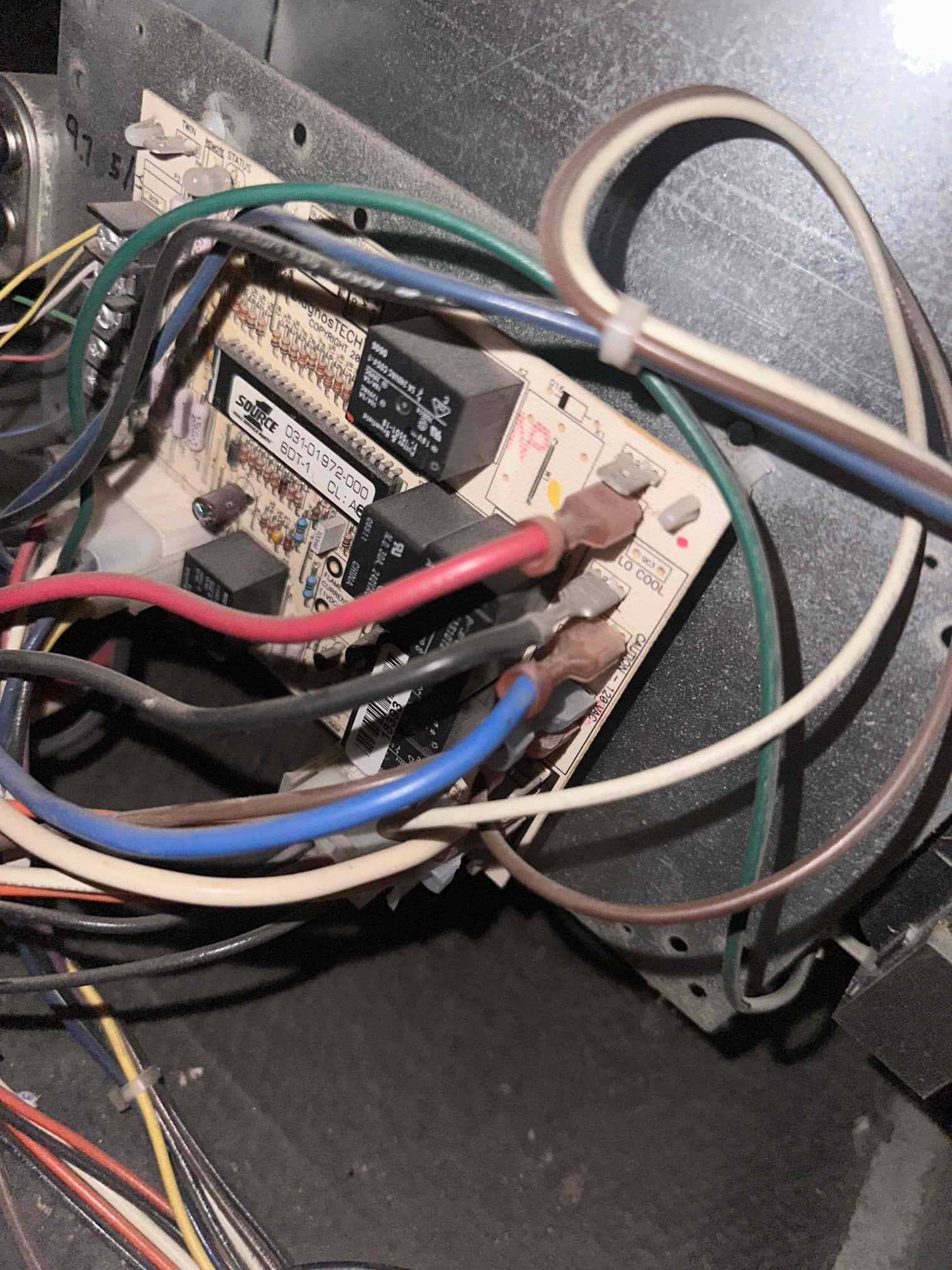HVAC control board with relays and components, showing multiple colored wires connected to labeled terminals inside the unit.