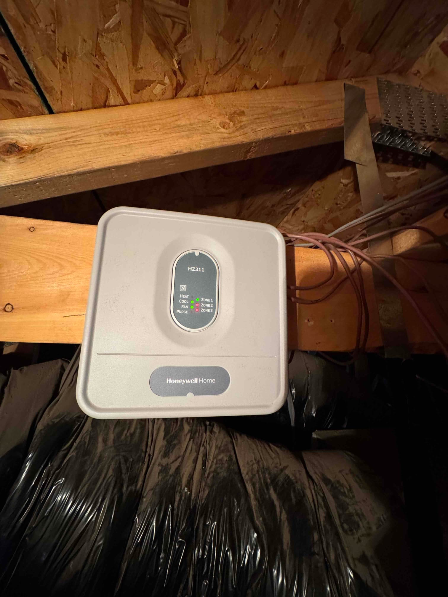 HVAC zone control panel with indicator lights mounted in the attic, with low-voltage wiring connected.