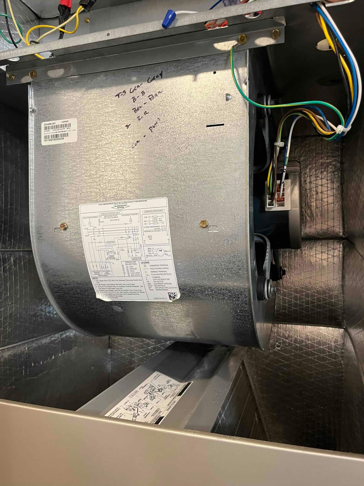 Indoor air handler blower assembly exposed, showing squirrel-cage blower, wiring harness, run capacitor, and wiring diagram stickers.