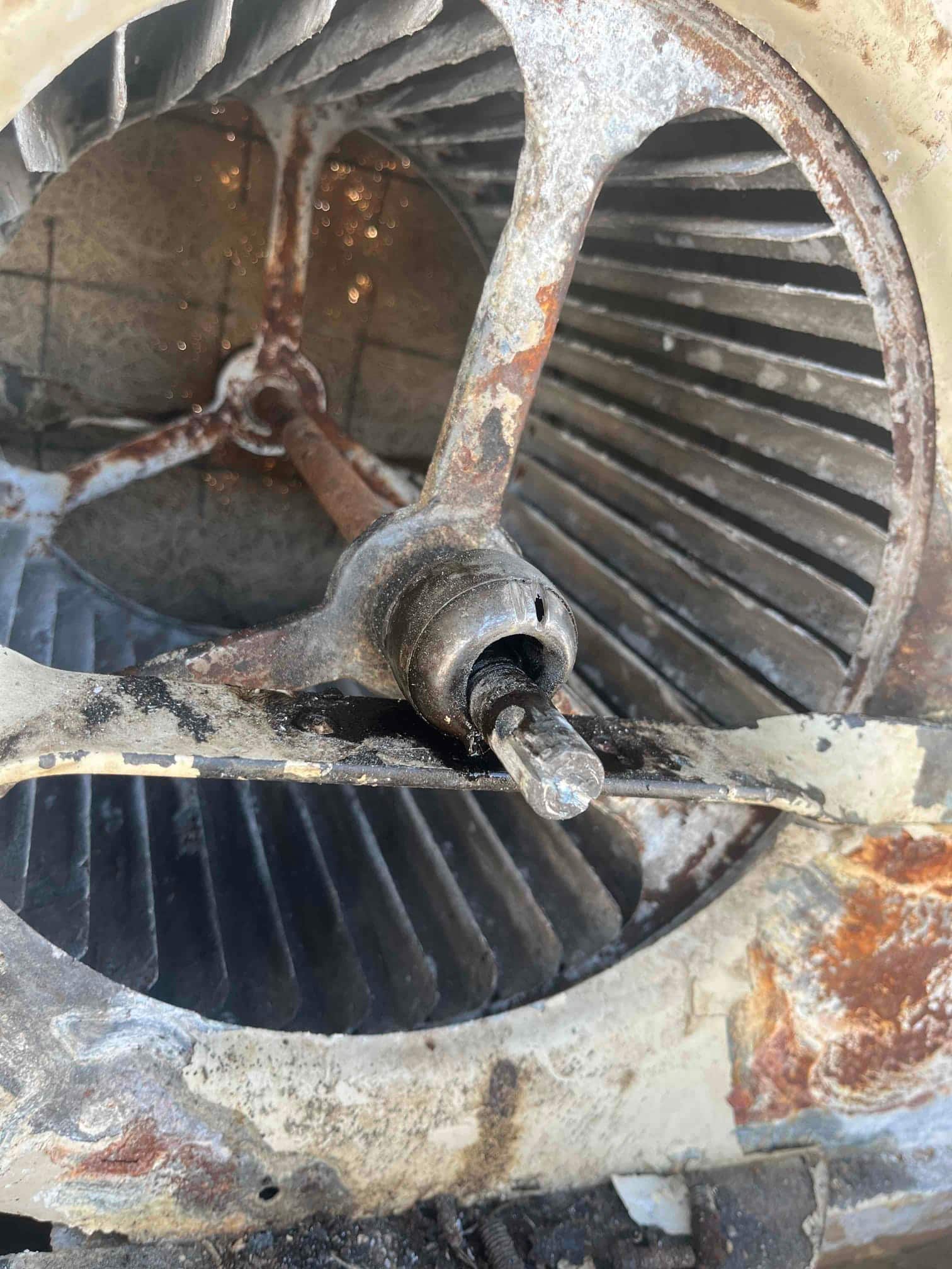 Indoor blower wheel and housing with rust, corrosion, and shaft exposed; accumulated dirt and debris present.