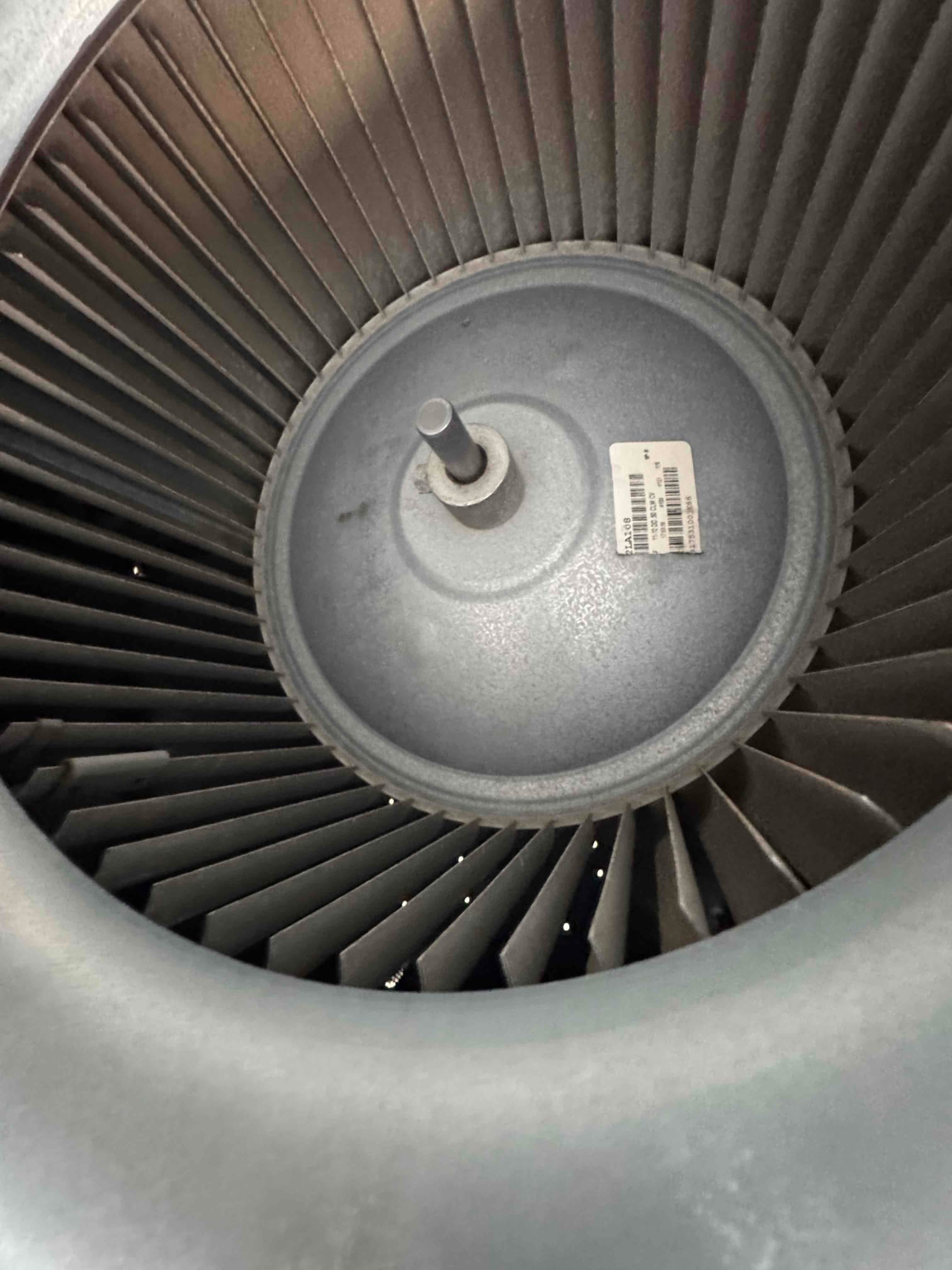 Indoor blower wheel and hub with central motor shaft visible, fins evenly spaced, and barcode label on the hub.