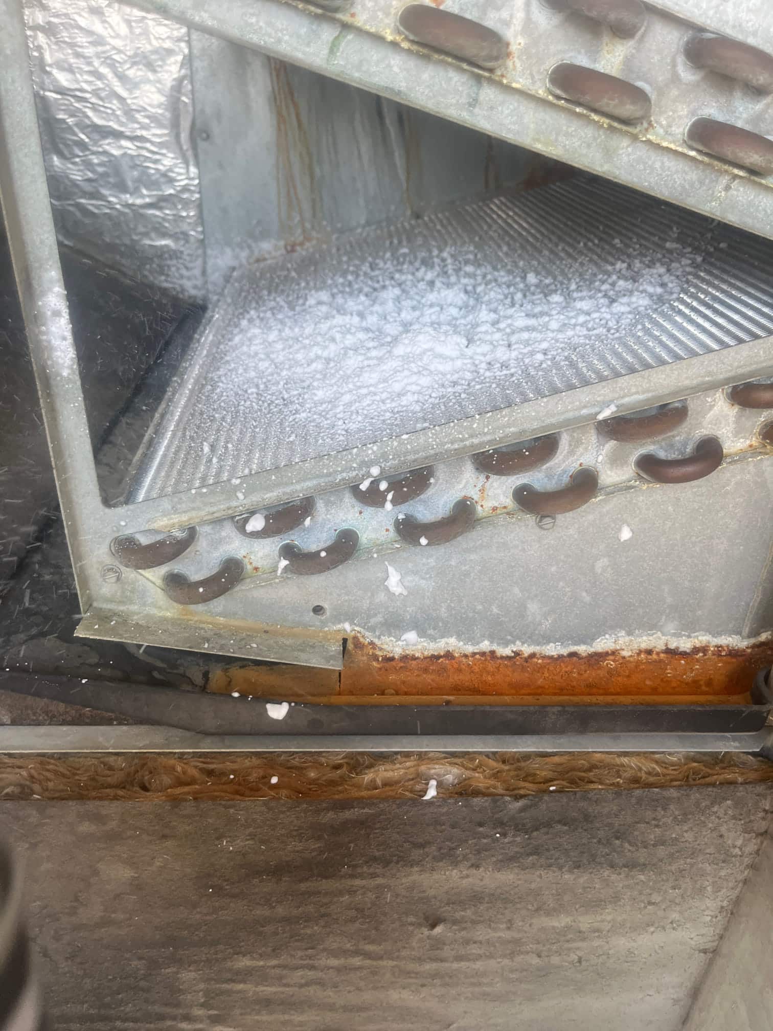 Indoor evaporator coil section with visible frost on fins and rust along drain pan edge.