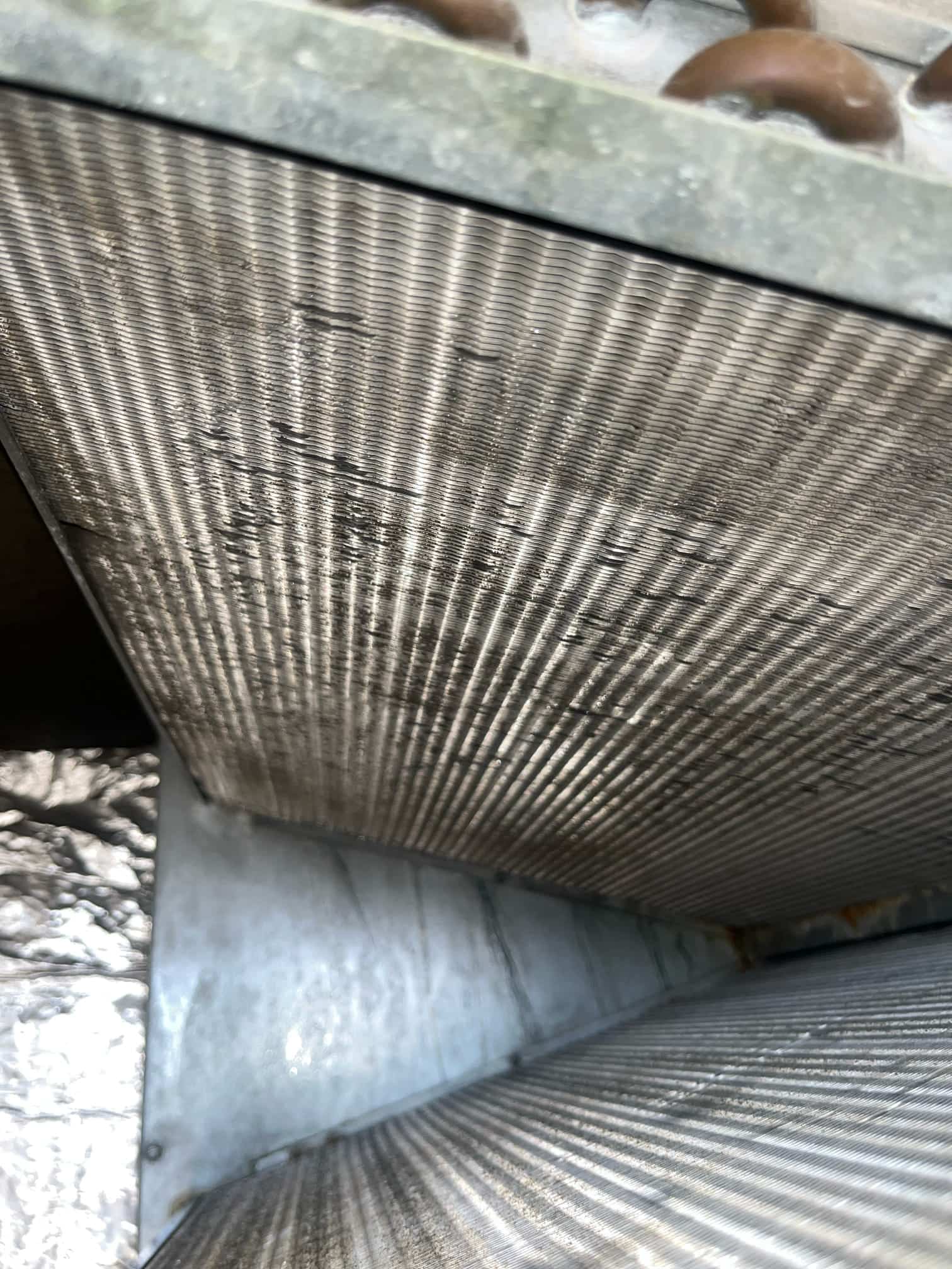 Inside view of an A-coil evaporator showing aluminum fins and copper tubes, with some bent fins and light debris.