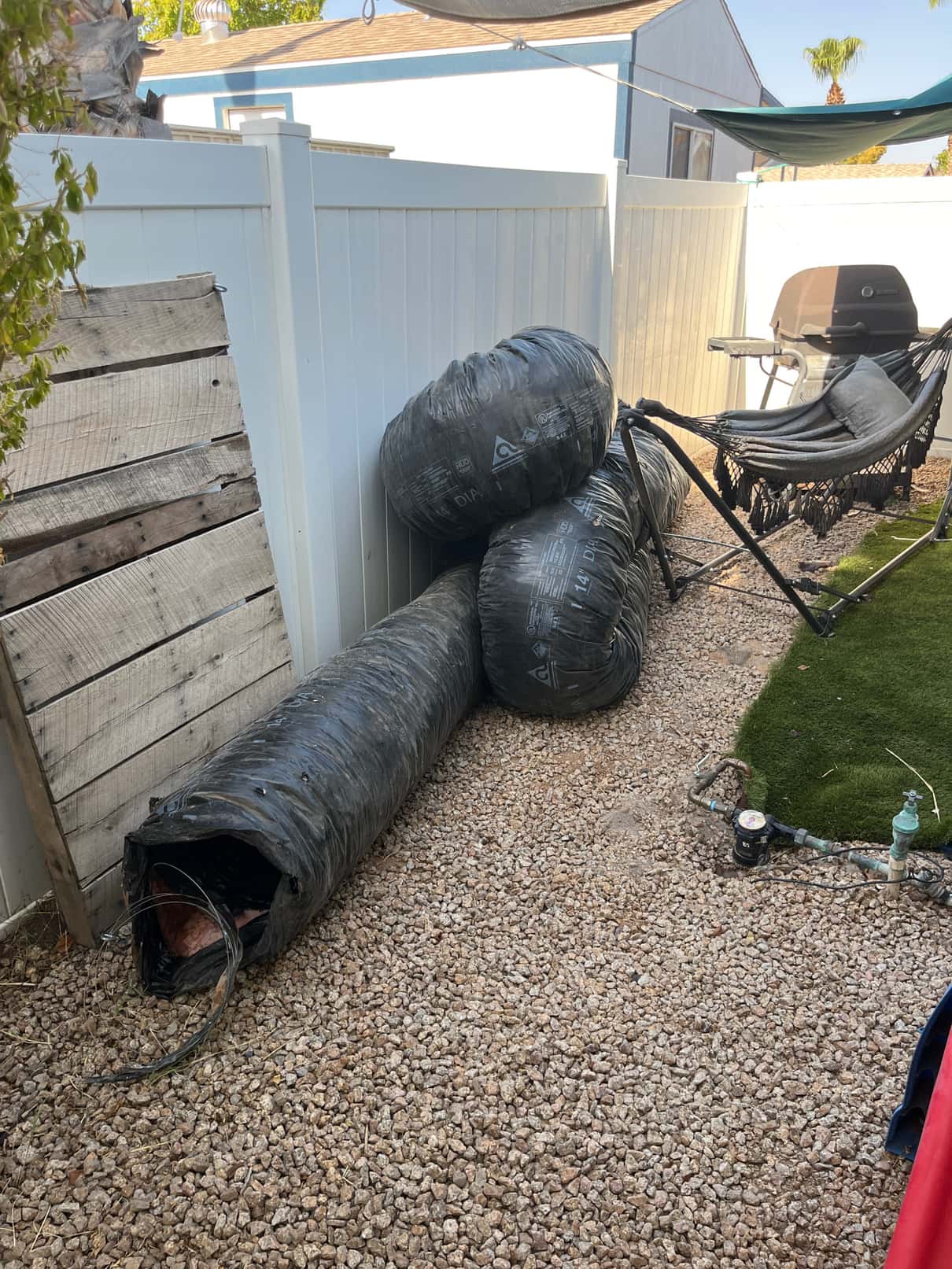 Insulated flexible air ducts removed and stacked outdoors beside a fence, showing torn ends.