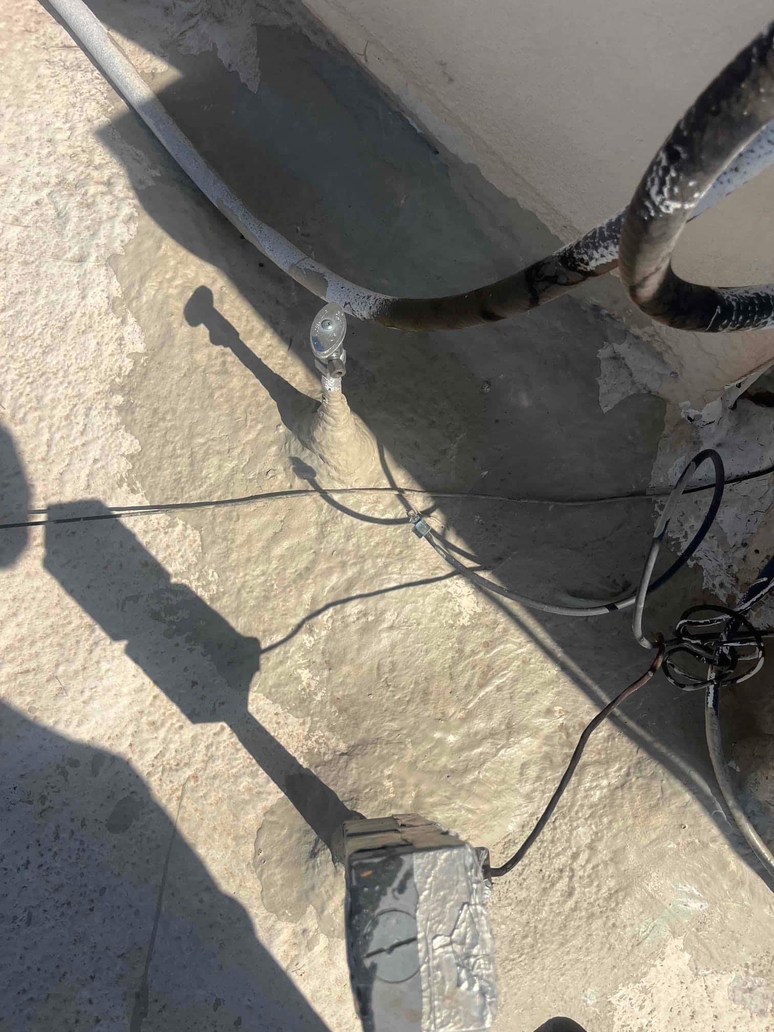 Insulated refrigerant lines and electrical wiring on a rooftop next to an exterior wall, with a metal box.