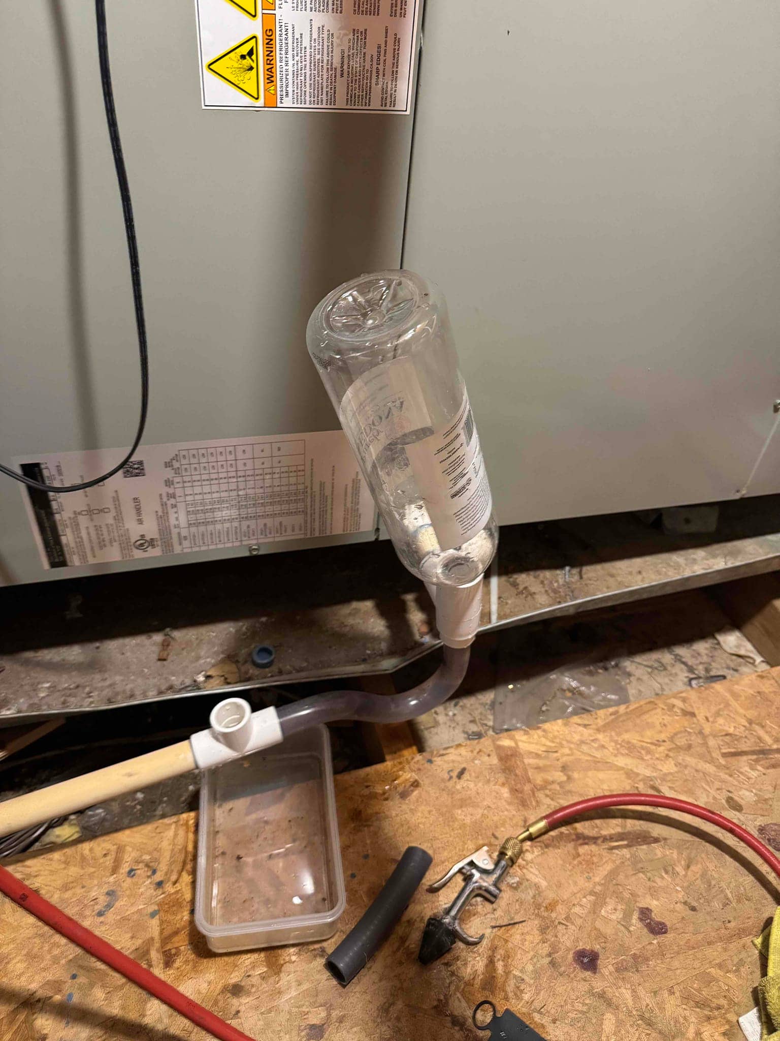 Inverted bottle inserted into the condensate drain assembly at the HVAC cabinet, with tubing and fittings.