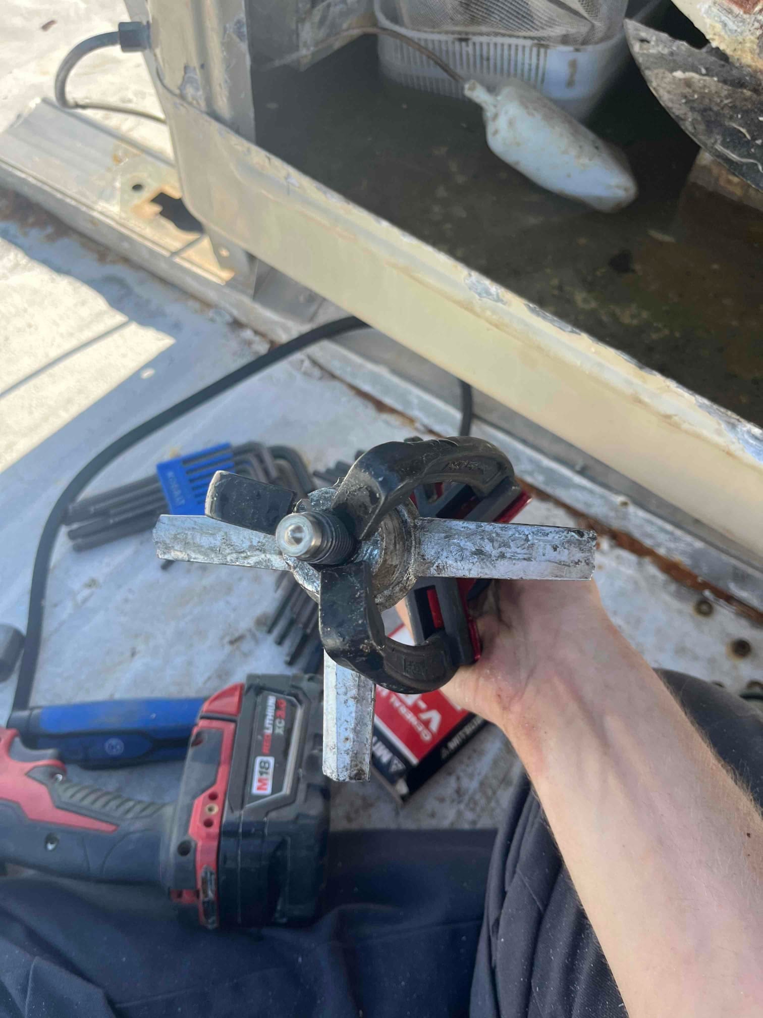 Three-jaw puller clamped on a shaft inside an HVAC unit cabinet, with hand tools visible around.