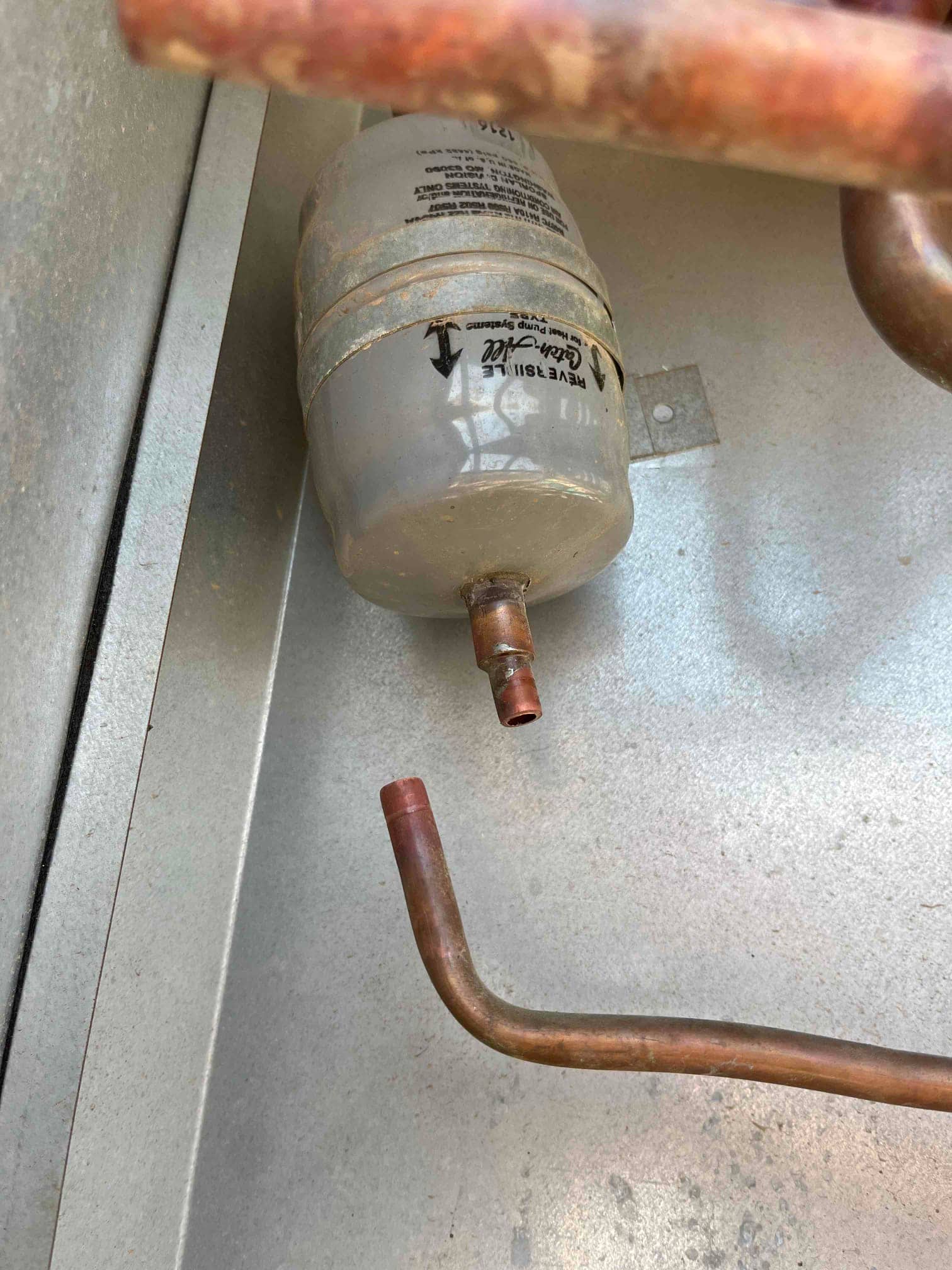 Liquid-line filter drier with copper refrigerant line disconnected at one end inside the condenser cabinet.