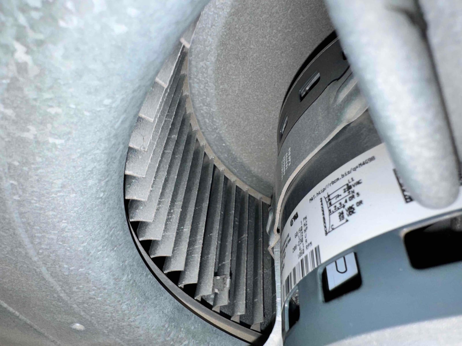 Metal blower wheel and attached motor inside the air handler housing, showing dust on the fins and manufacturer label.
