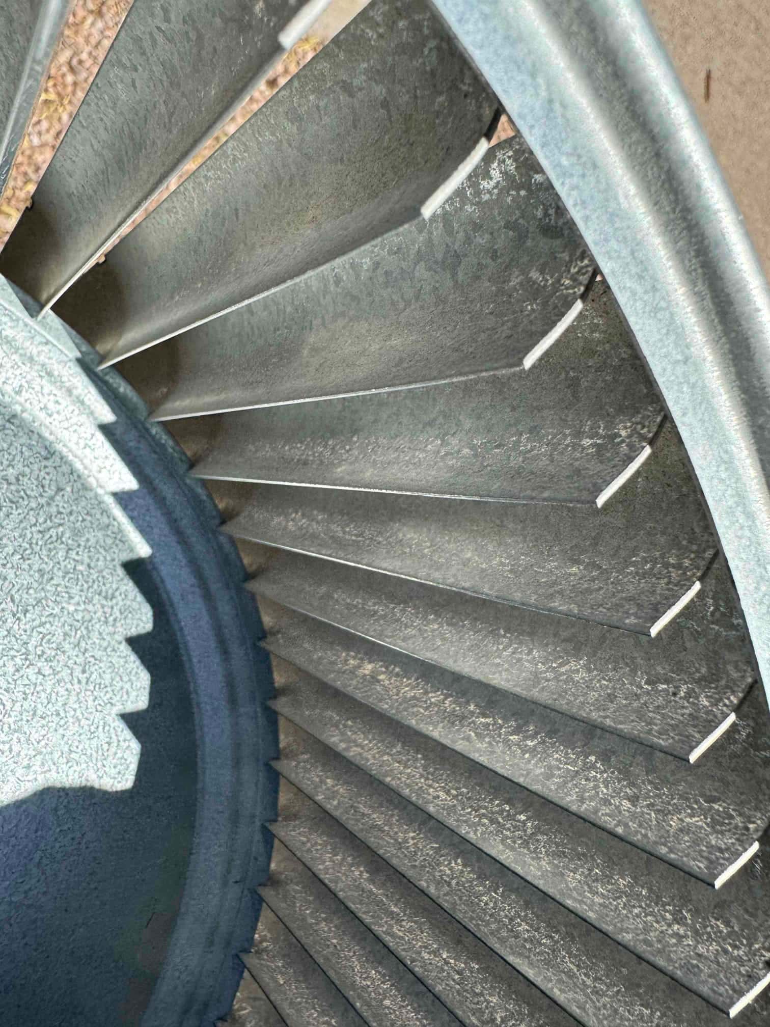 Metal centrifugal blower wheel with multiple vanes, showing light surface dust on blades.