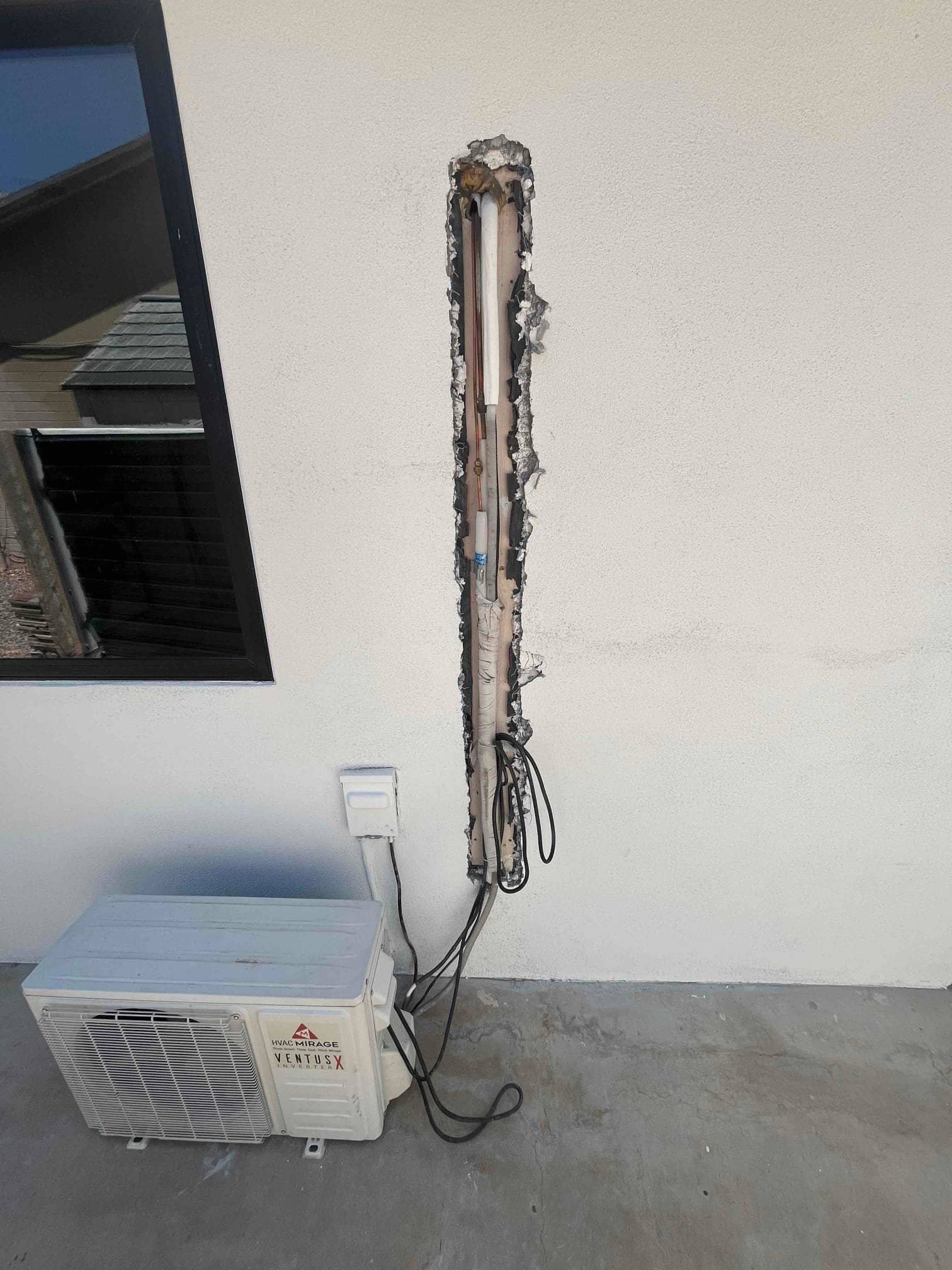 Mini-split outdoor unit below an open wall chase, showing exposed refrigerant lines, insulation, drain tube, and electrical wiring.