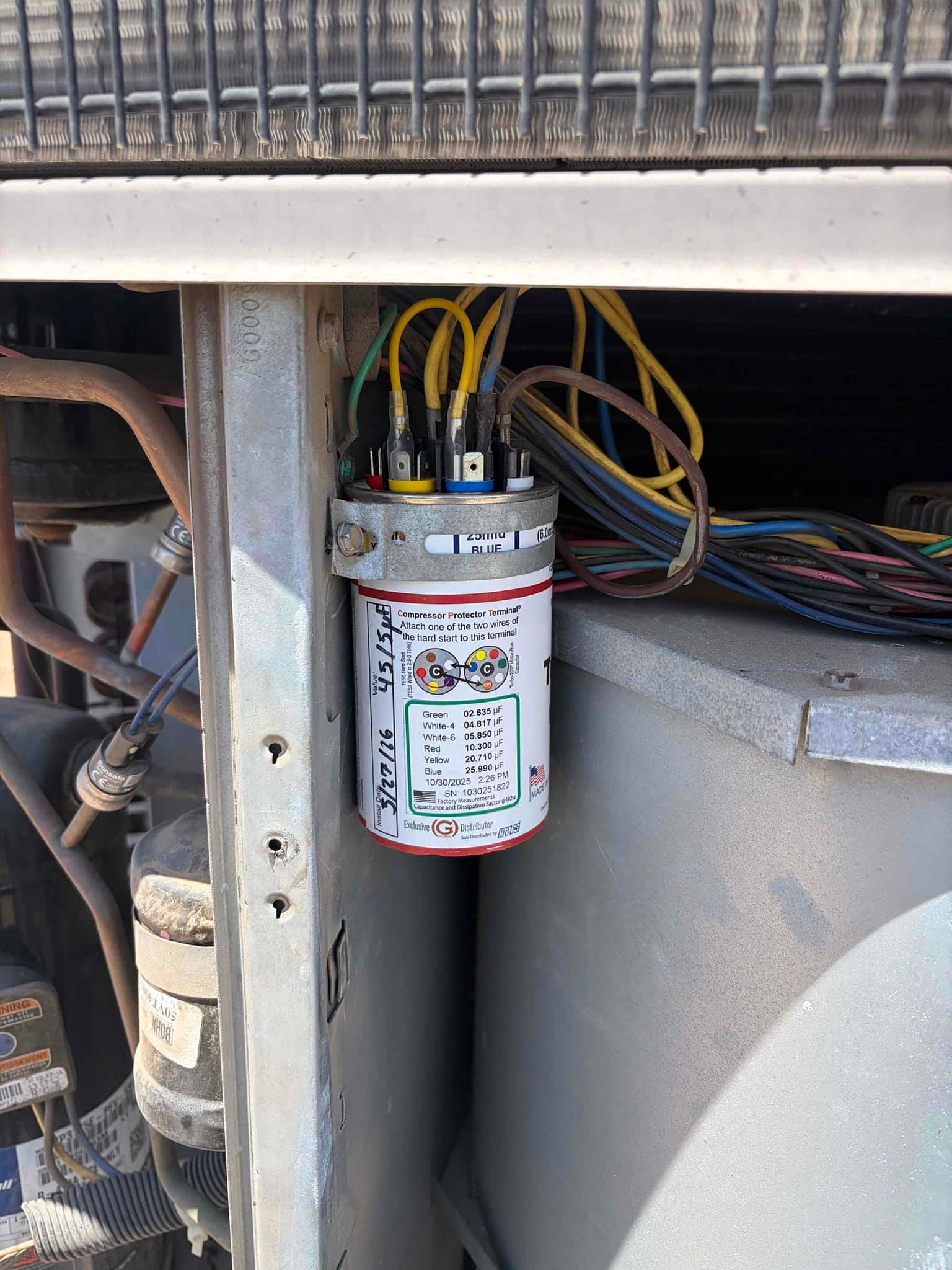 Multi-tap run capacitor with color-coded terminals and connected wires mounted inside the outdoor condenser cabinet near the fan housing.