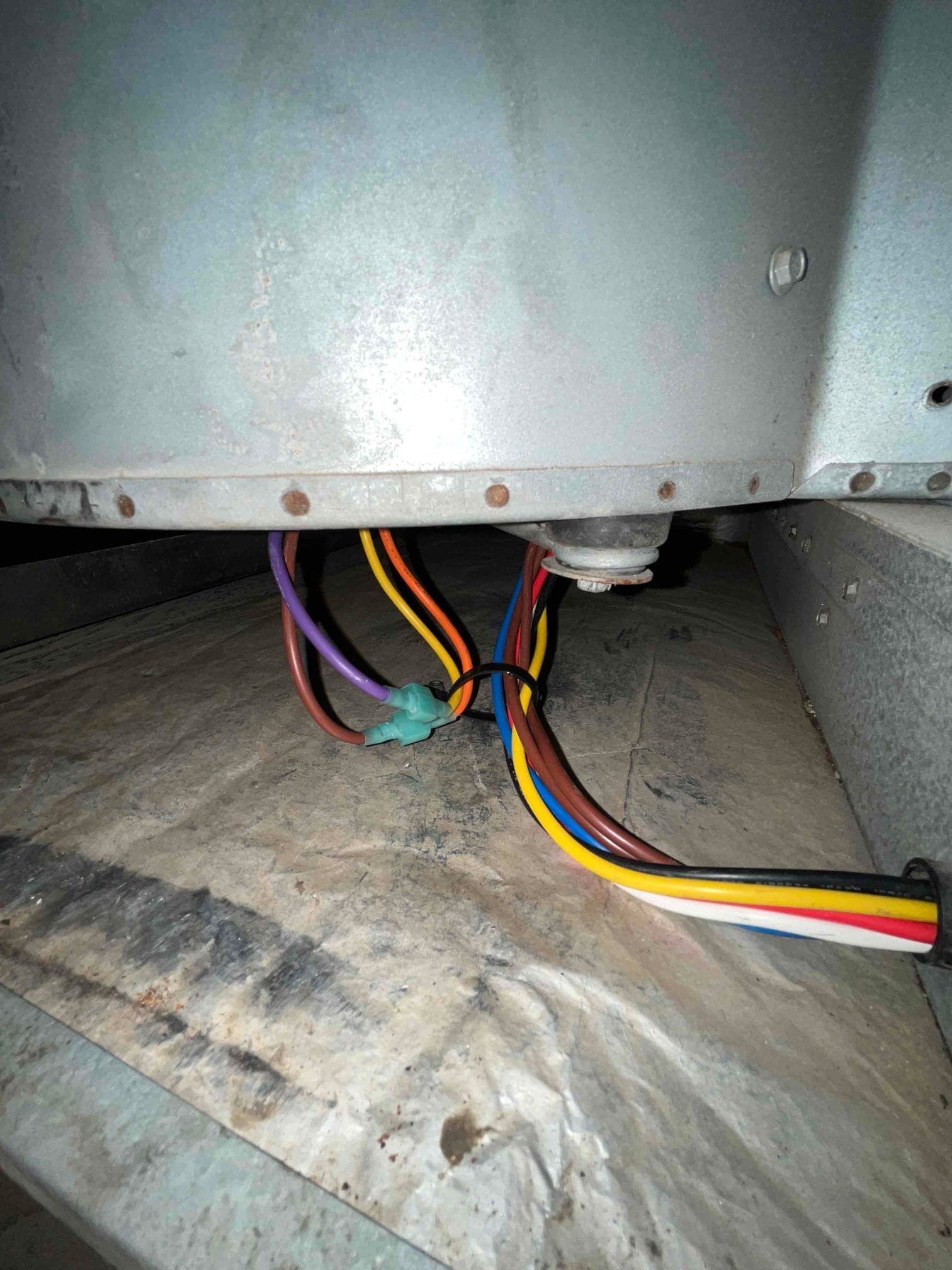 Multicolor wires exit a grommet beneath an HVAC cabinet, joined by a green connector and zip tie.