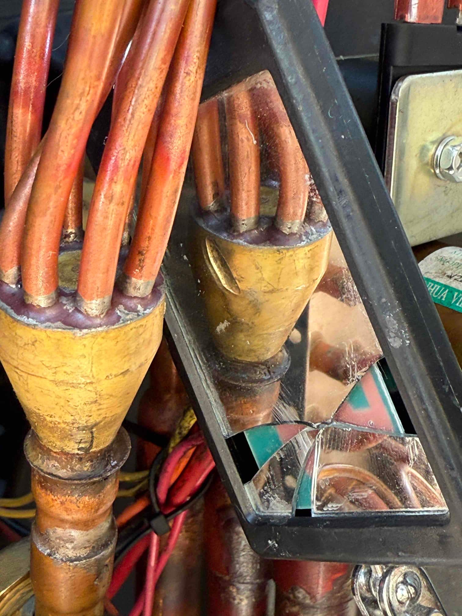 Multiple small copper refrigerant tubes enter a sealed brass manifold, with a broken inspection mirror positioned for viewing tight areas.