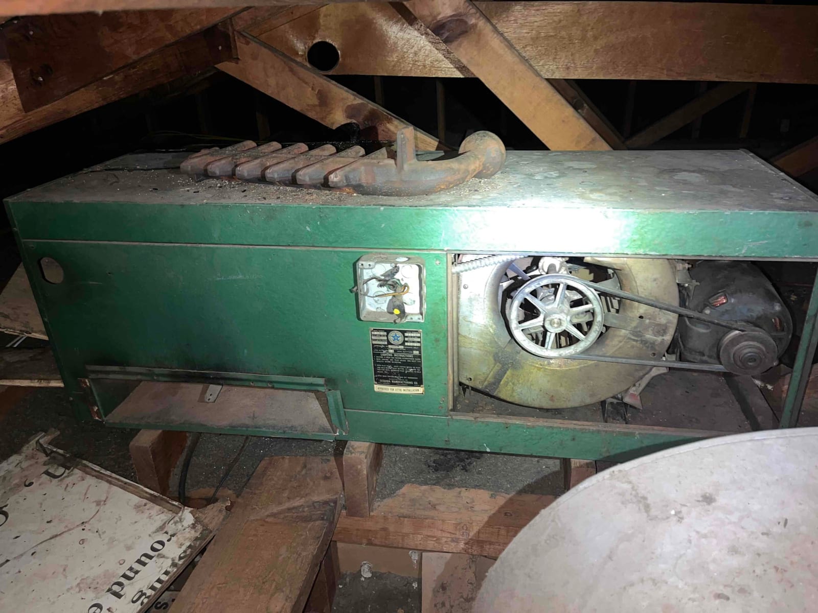 Older attic-mounted air handler with belt-driven blower assembly exposed, showing motor, pulley, and accumulated dust on the housing.