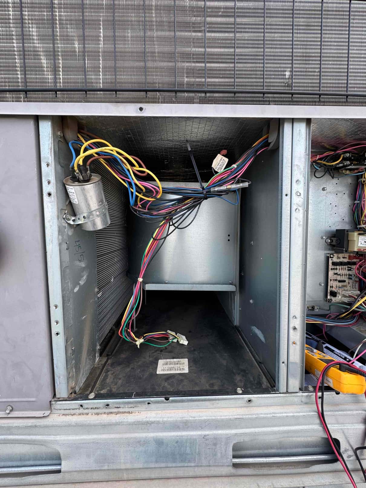 Open air handler compartment showing blower housing, run capacitor with connected wiring, and control board with harnesses accessible for service.