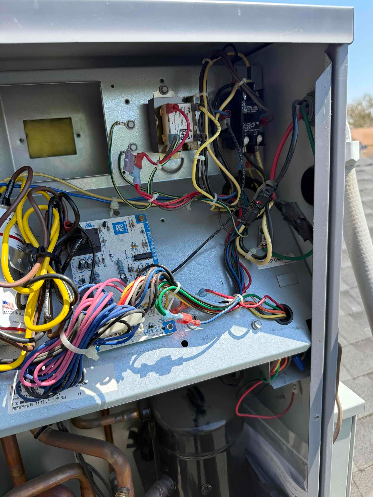 Open condenser control compartment showing contactor, transformer, control board, and bundled wiring above the compressor and copper refrigerant lines.