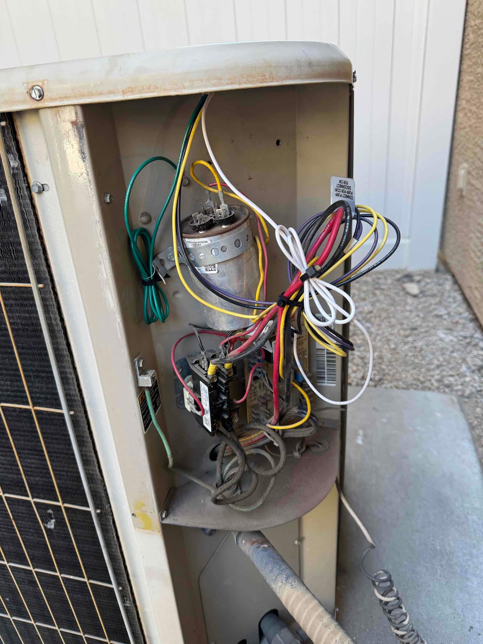 Open condenser control compartment showing a run capacitor, contactor, and connected wiring, with dust on interior surfaces.