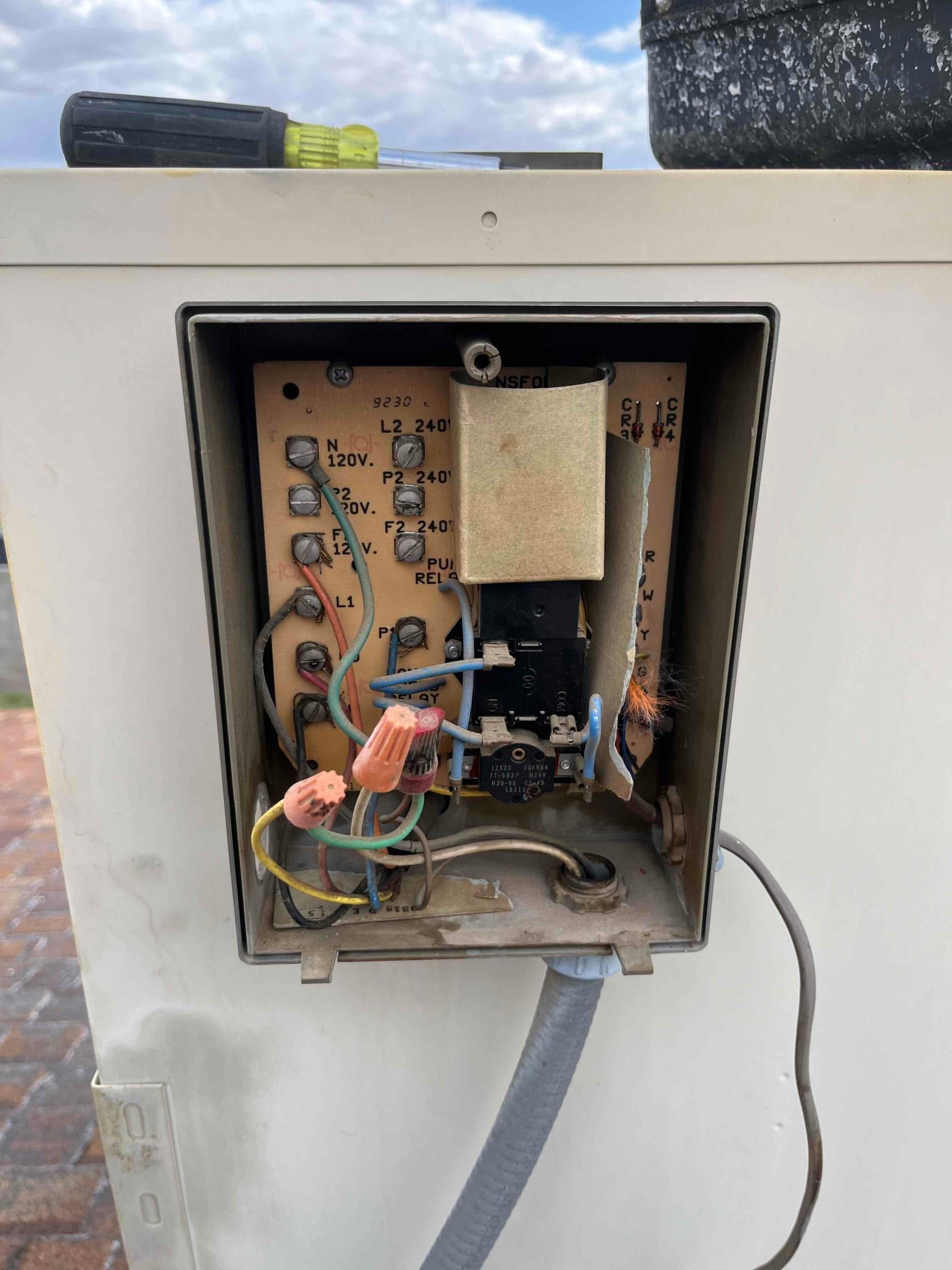 Open outdoor condenser control compartment showing wiring, terminal block labels, relay, transformer, and wire nuts.