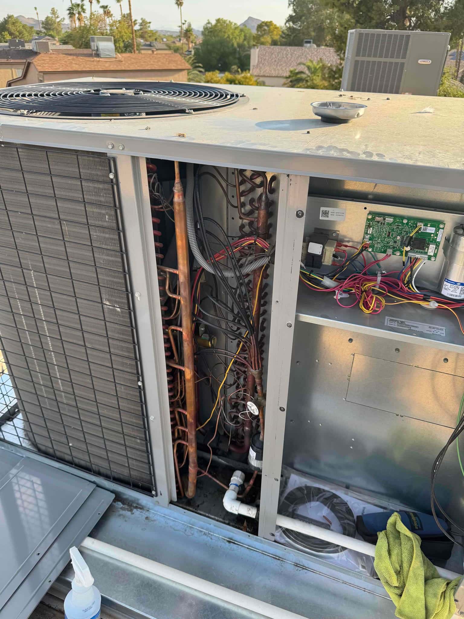 Open outdoor HVAC unit cabinet showing copper refrigerant lines, coil tubing, control board, wiring, and condensate drain piping.
