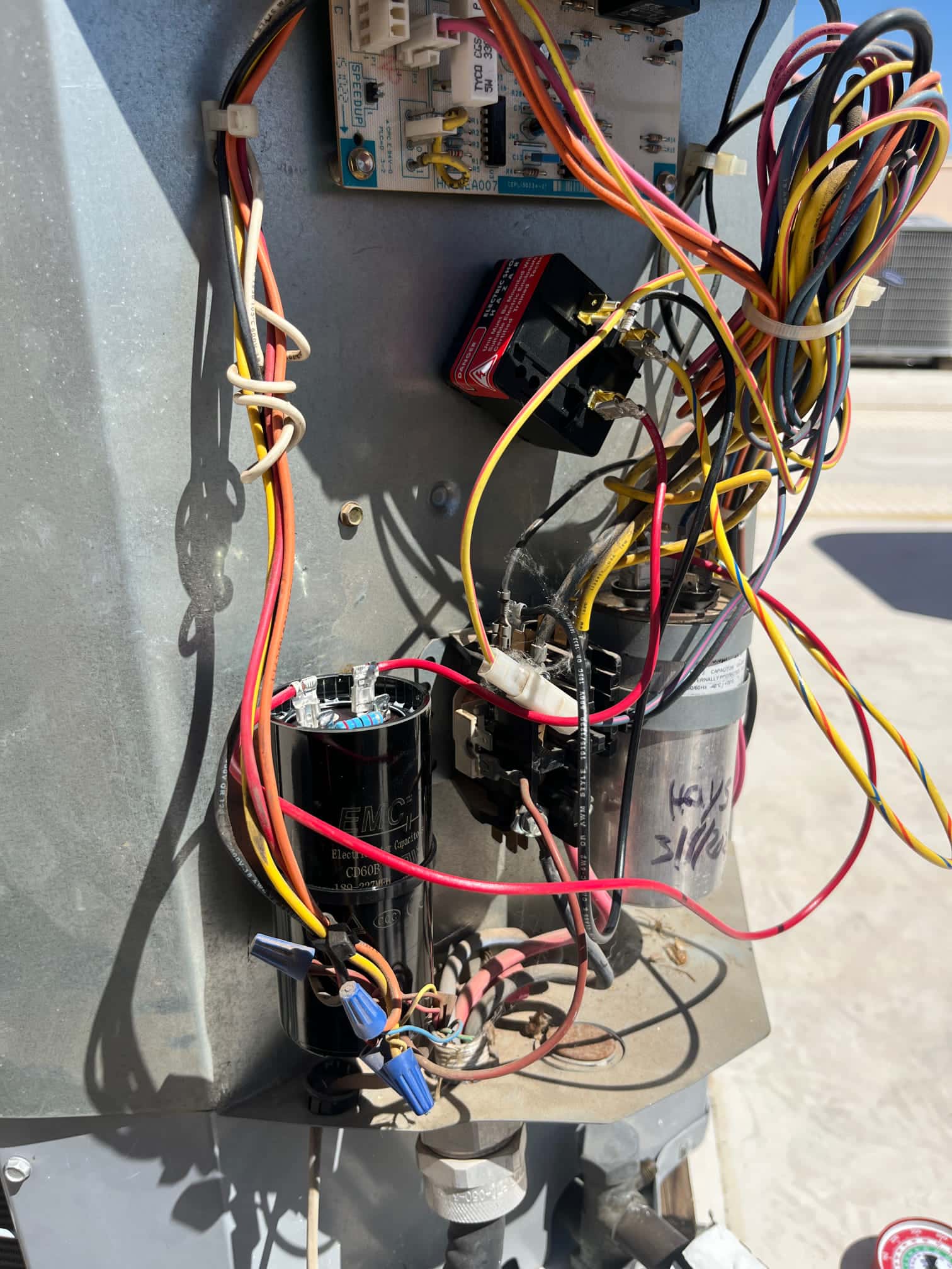 Open outdoor unit control compartment showing two run capacitors, a contactor, control board, and multiple connected wires.