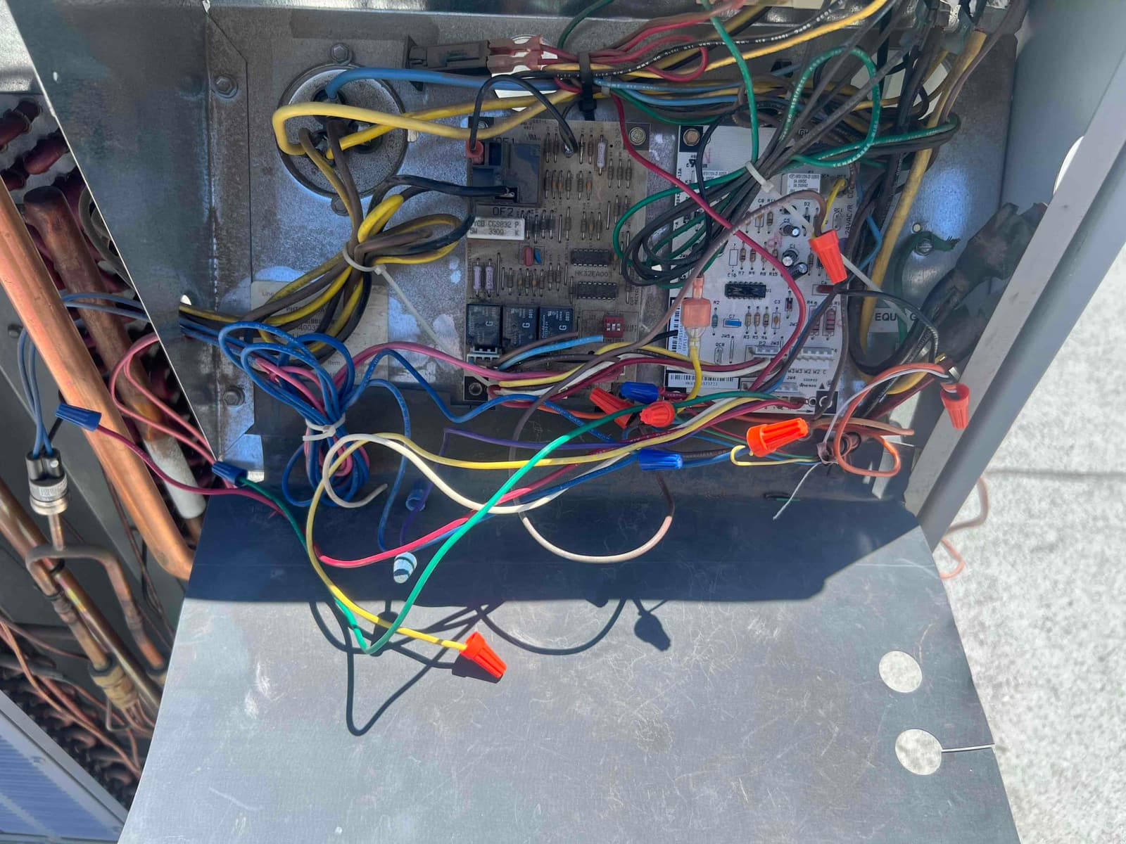 Open outdoor unit control compartment shows circuit boards, numerous colored wires with wire nuts, and copper refrigerant lines at left.