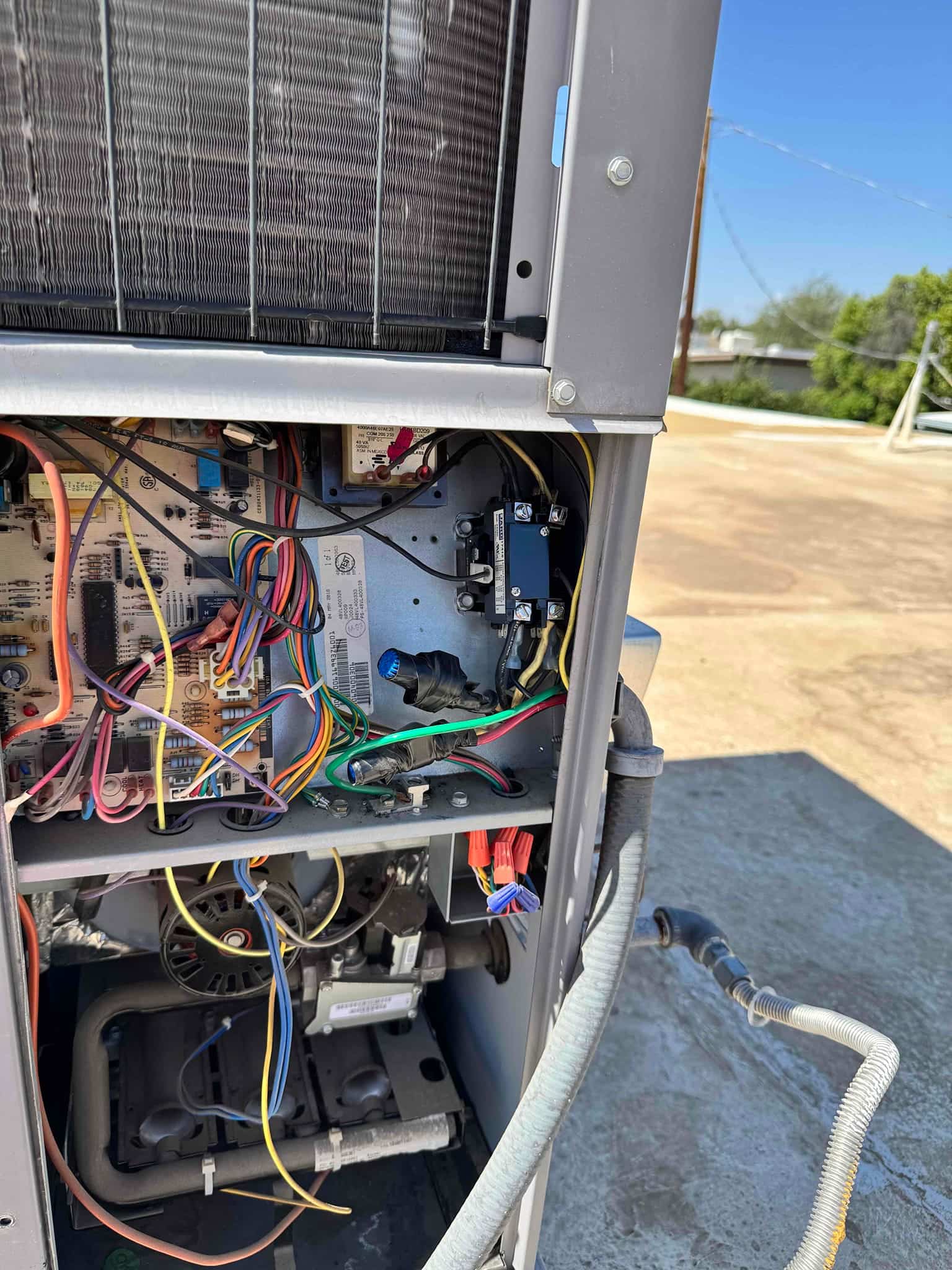 Open service panel shows control board, wiring harnesses, relay, inducer motor, and burner assembly inside rooftop unit.
