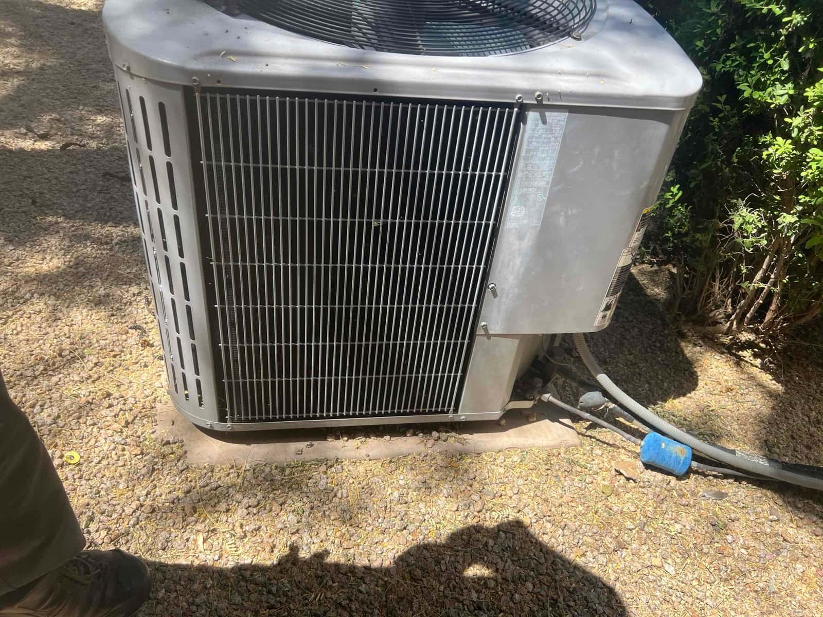 Outdoor air conditioner condenser unit on gravel pad with refrigerant lines and disconnect whip attached.