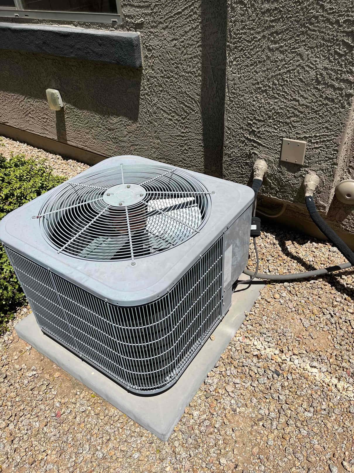 Outdoor air conditioning condenser unit on pad beside house, with insulated refrigerant lines entering wall.