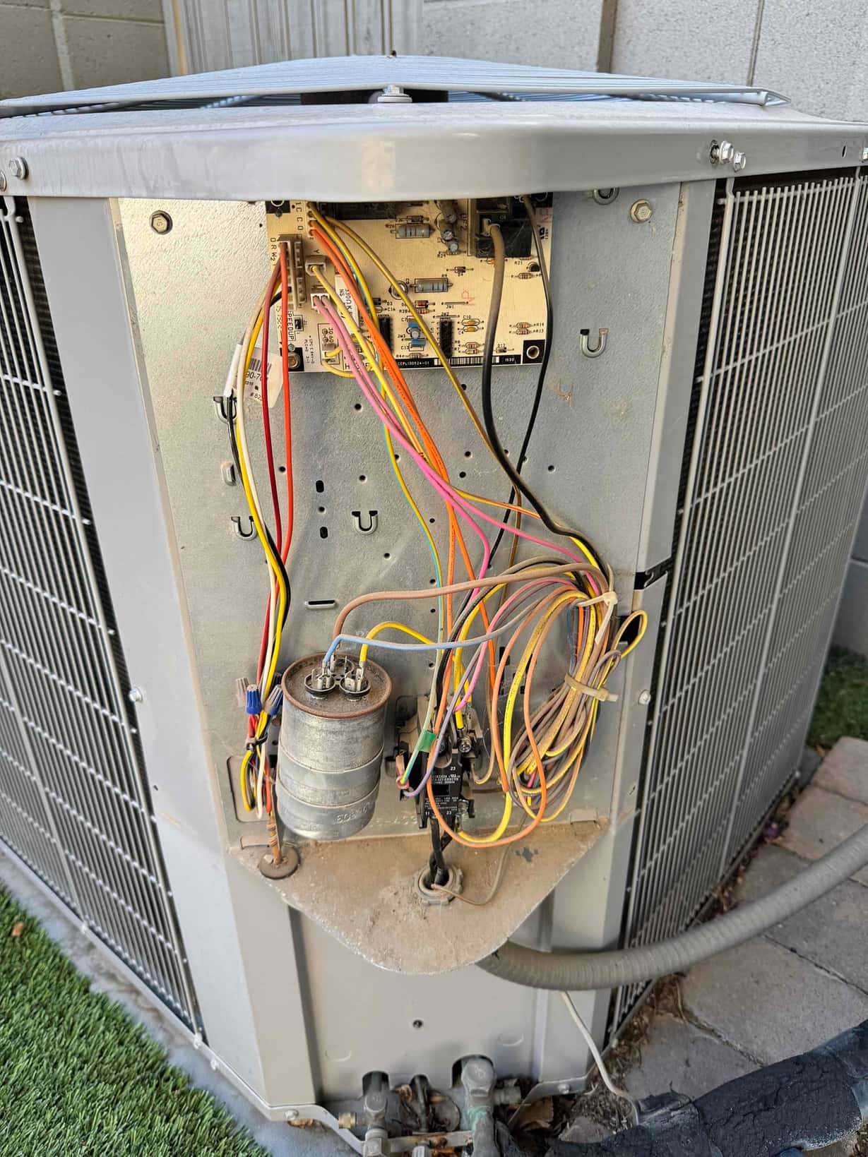 Outdoor condenser access panel open, showing dual-run capacitor, contactor, control board, and multiple connected wires and terminals.
