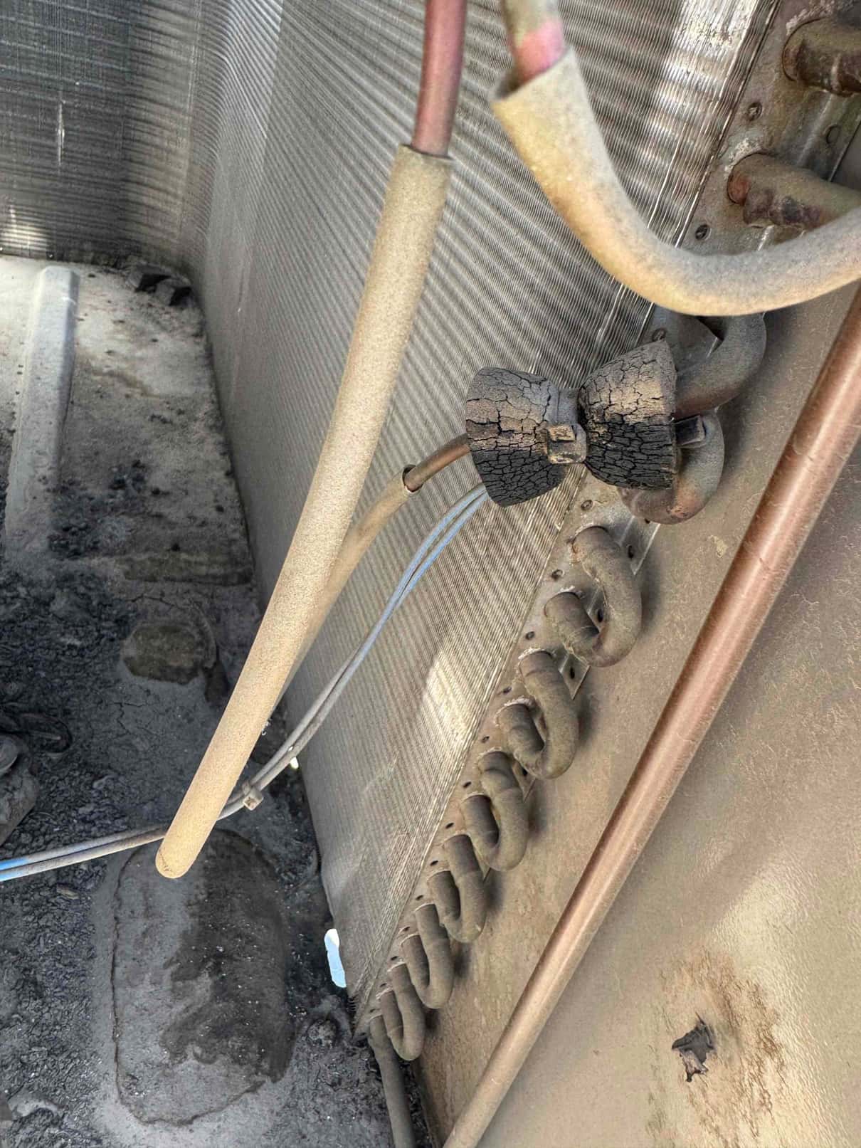 Outdoor condenser coil interior showing copper refrigerant lines, return bends, and cracked, deteriorated insulation around a tubing section.