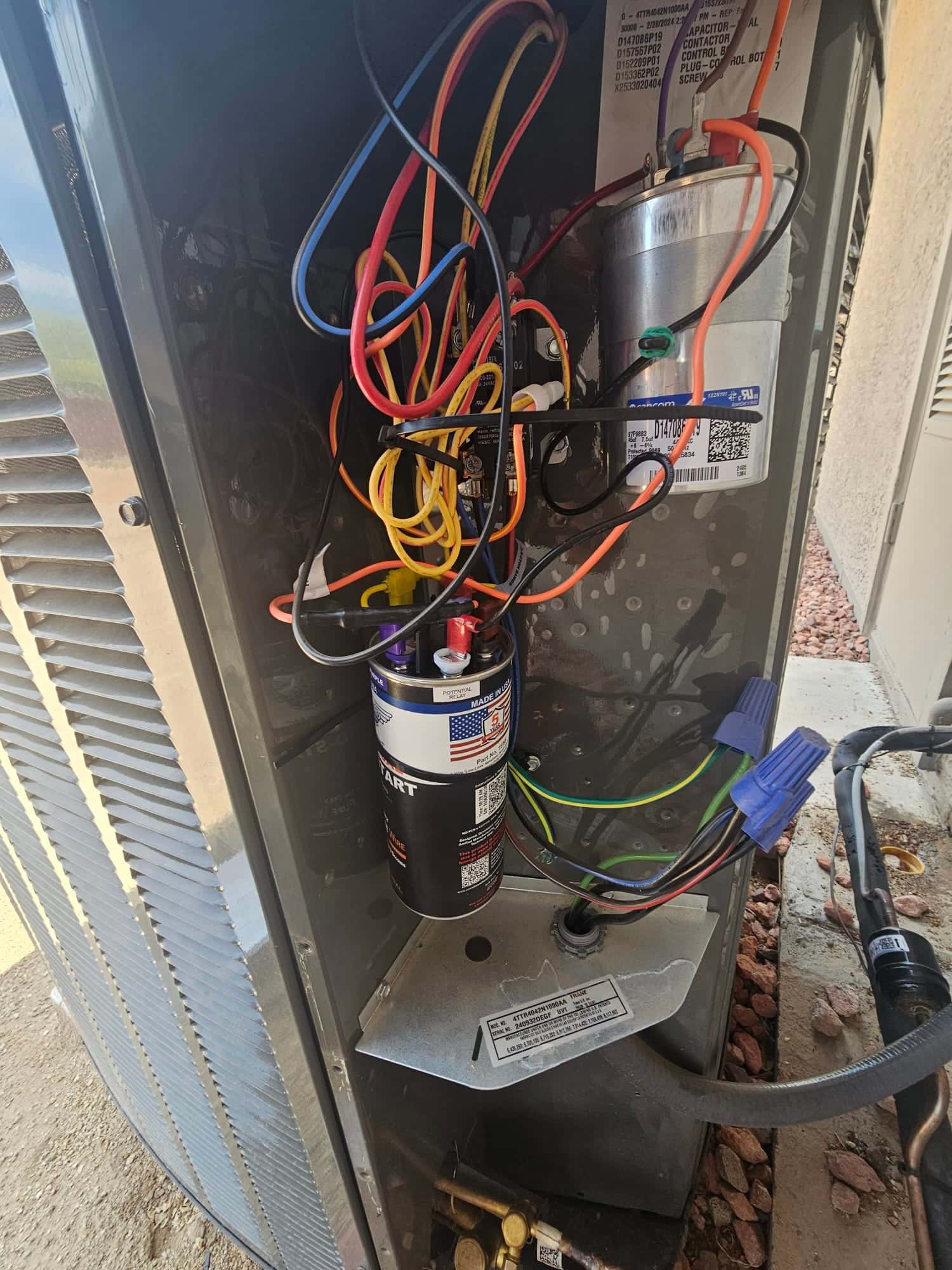 Outdoor condenser control compartment with a dual-run capacitor, hard start kit, wire nuts, and connected wiring.