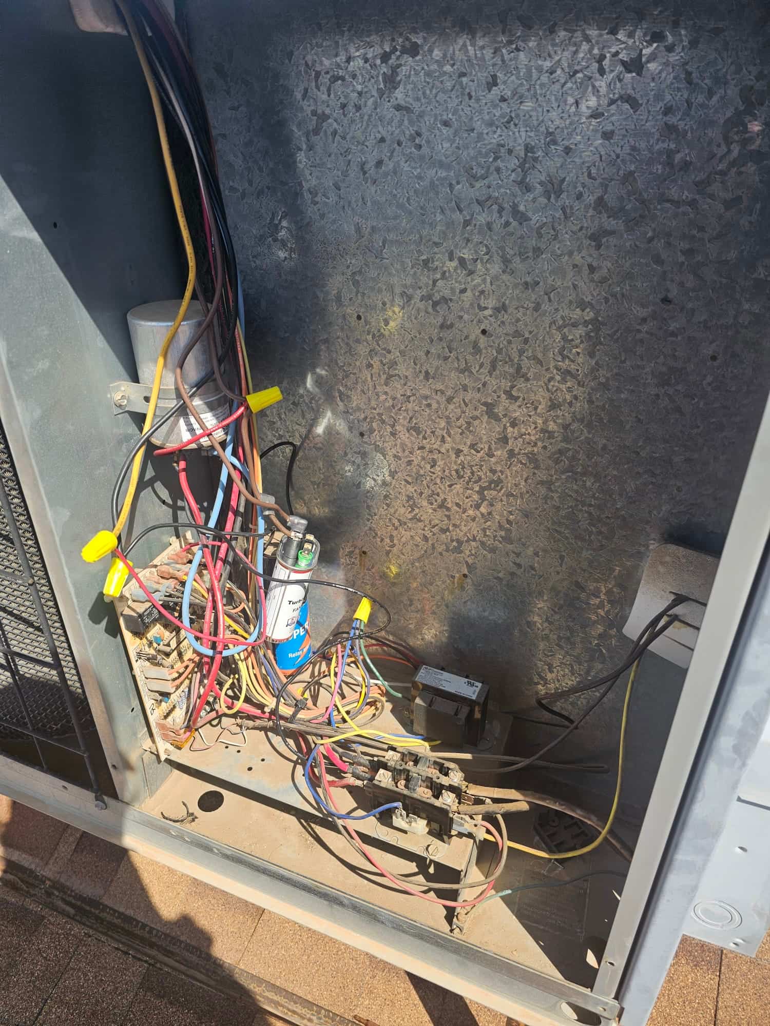 Outdoor condenser electrical compartment showing a run capacitor, contactor blocks, and numerous connected wires with wire nuts.