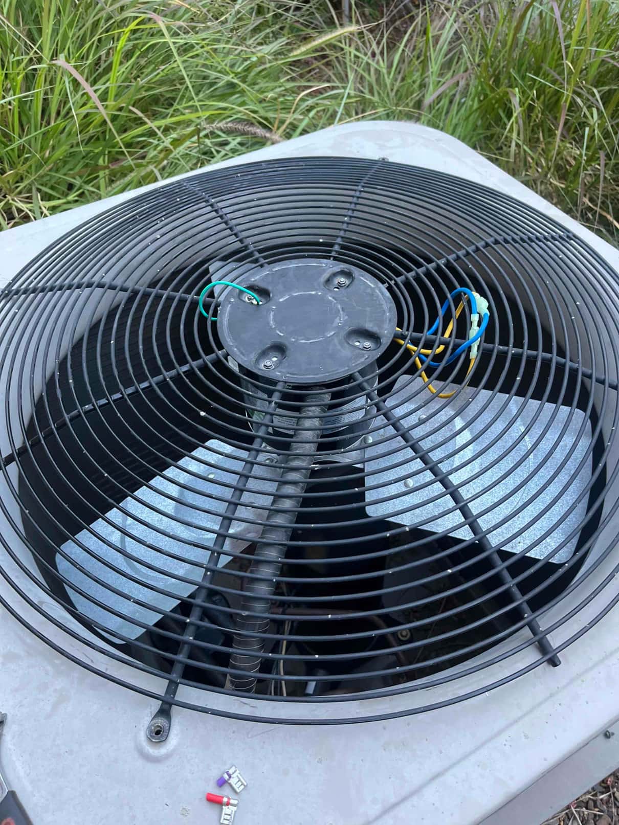 Outdoor condenser fan assembly with protective grille, motor top and wiring; loose crimp terminals rest on the unit cabinet.