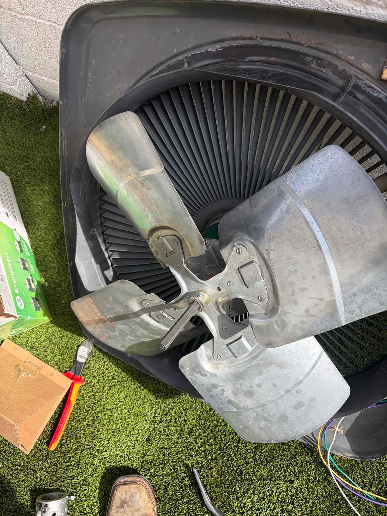 Outdoor condenser fan blade and top shroud removed, with wiring and tools visible on the ground.