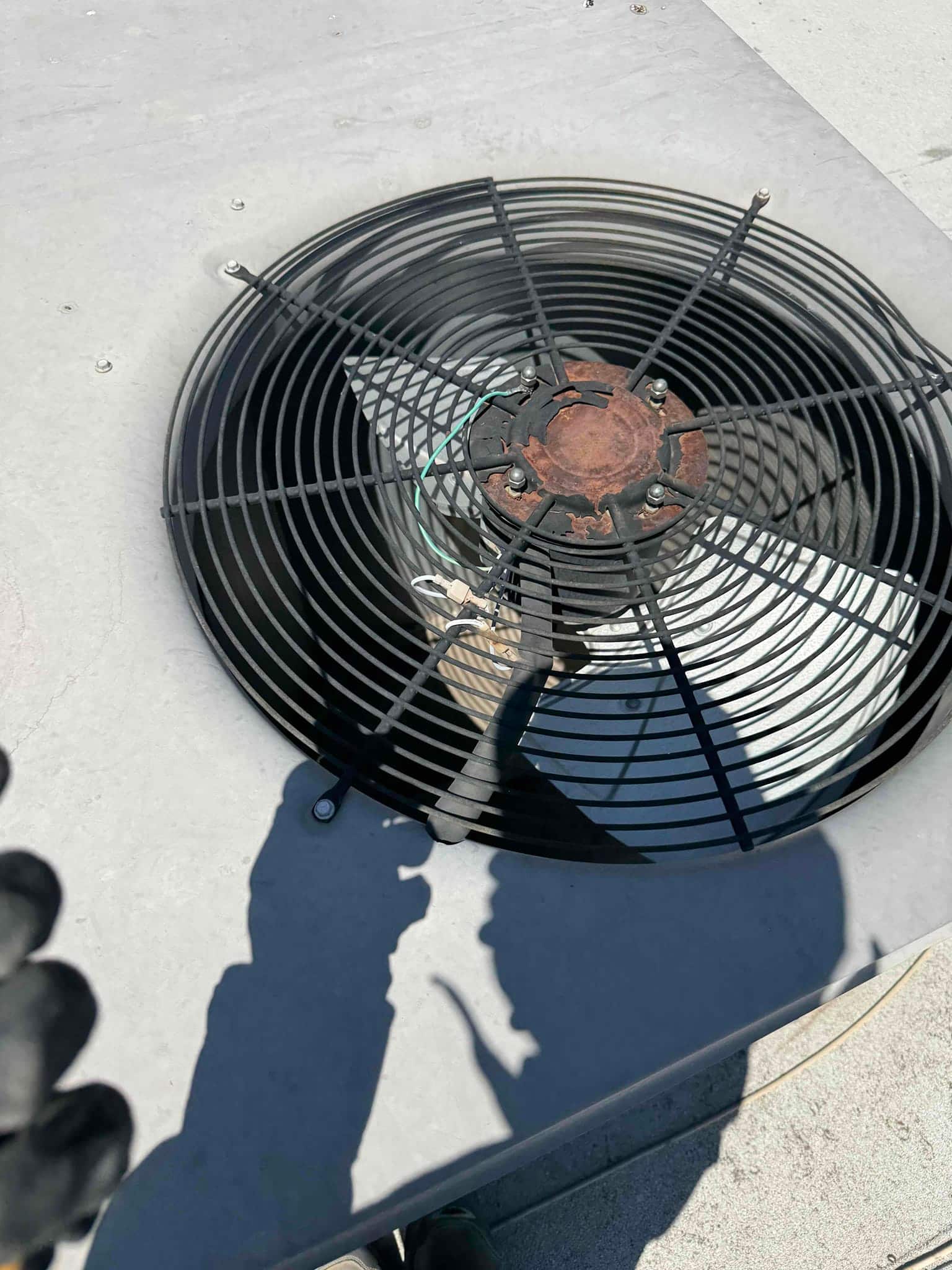 Outdoor condenser fan grille with a rusted fan hub and mounting hardware visible on the unit top.