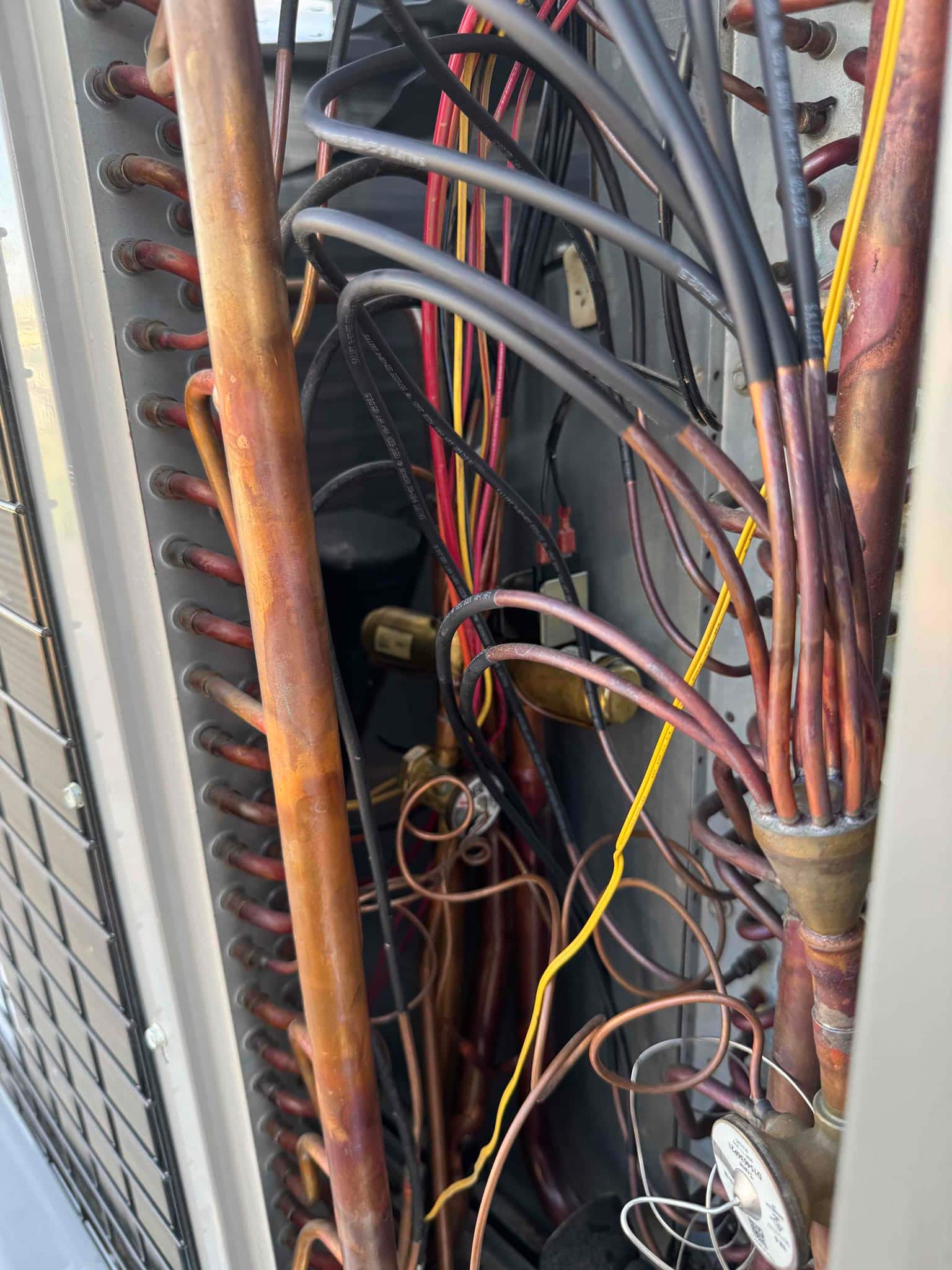 Outdoor condenser interior shows copper refrigerant piping, coil return bends, distributor with capillary tubes, and bundled control wiring.