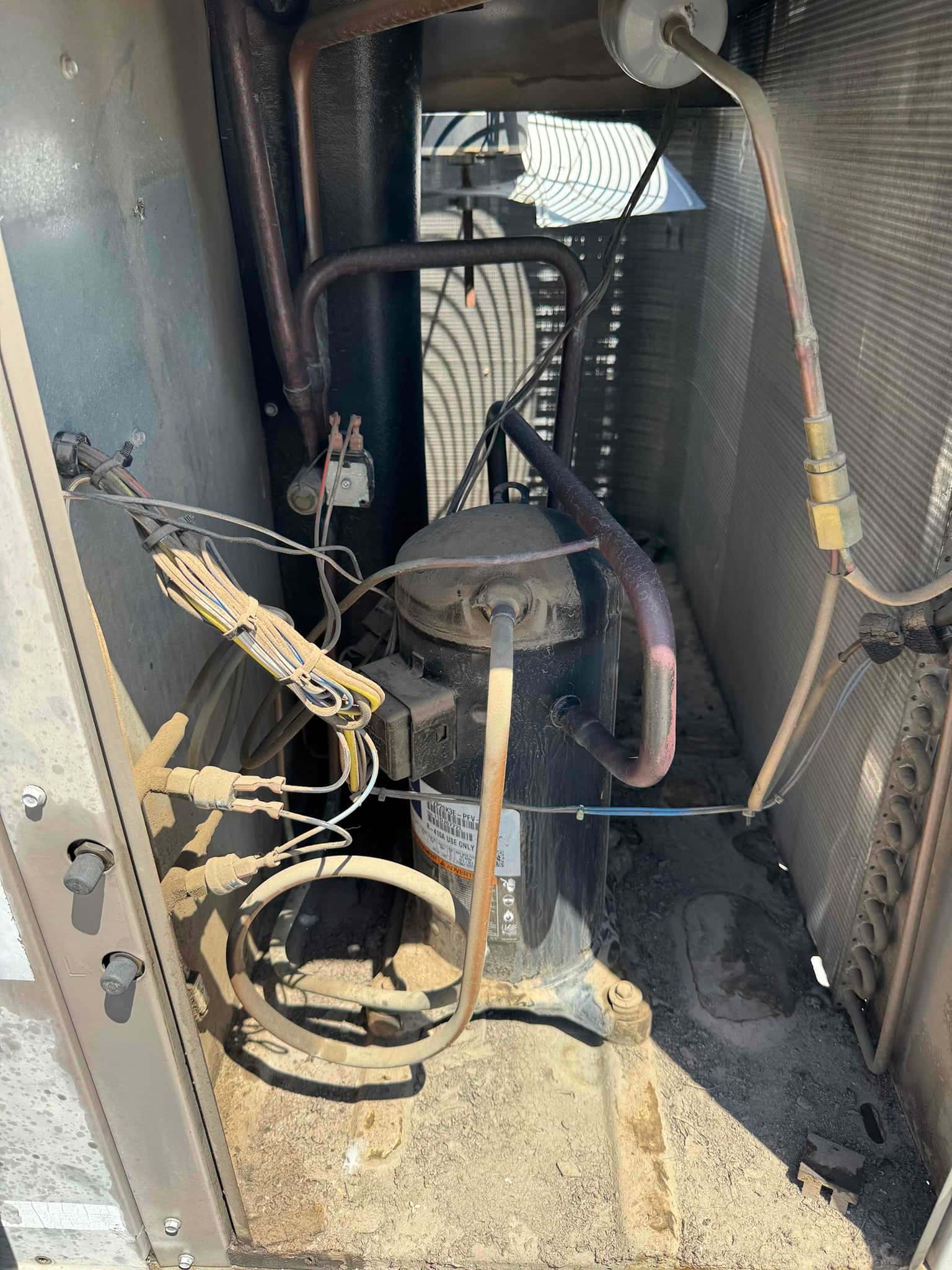 Outdoor condenser interior shows a hermetic compressor, copper refrigerant lines, service ports, and wiring with accumulated dust.